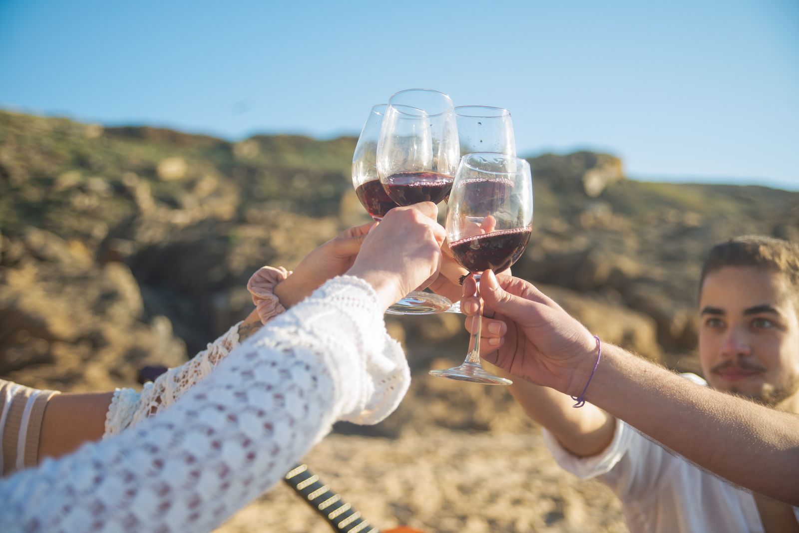 Tres amigos brindando con copas de vino tinto en un paisaje seco y rocoso. Foto de Kampus Production en Pexels.