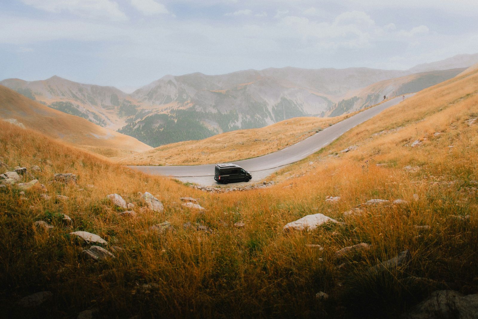 A van on a road curving through bare golden hills. Photo by Daniel J. Schwarz on Pexels.
