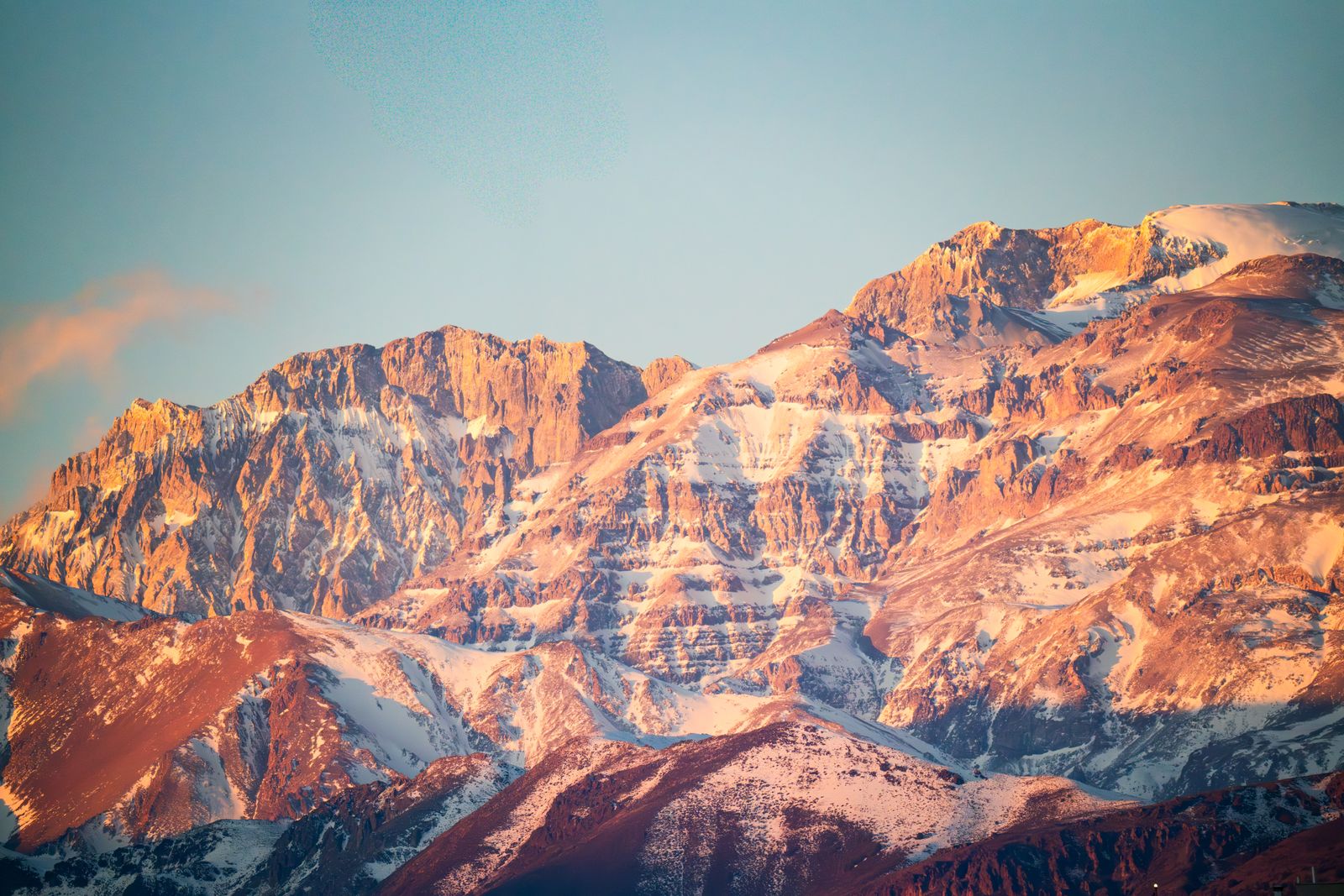 A high rock wall in the Andes lit orange by low sun. Photo by Hernan Berwart on Pexels.