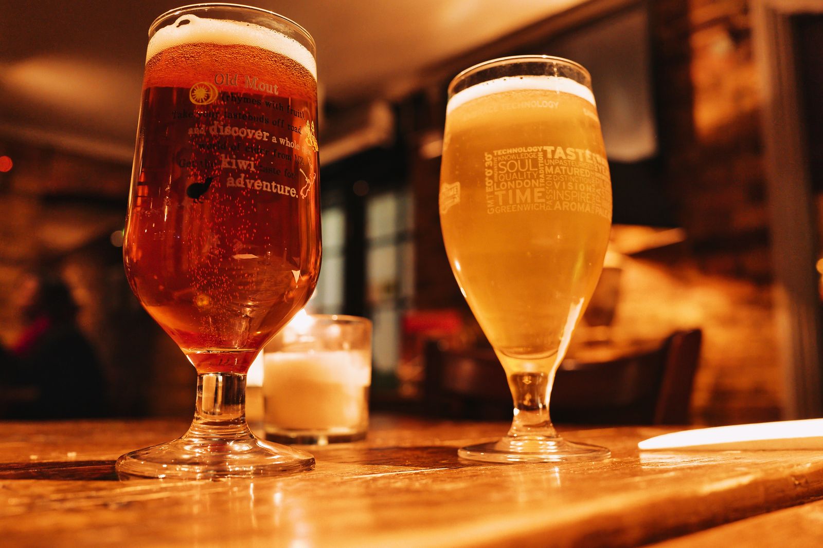 Two glasses of beer on a wooden table in a warm, low-lit room. Photo by Fernando B M on Pexels.