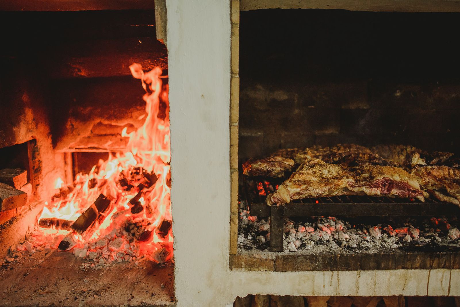 Un corte grande de carne cocinandose despacio junto a las brasas en un hogar de piedra. Foto de Lucas Gramatica en Pexels.