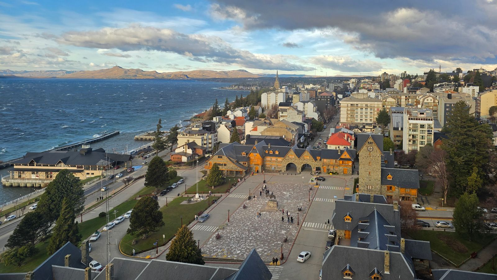 Los edificios de piedra y la plaza abierta del Centro Civico de Bariloche desde arriba, con el lago al fondo. Foto de Belén Montero en Pexels.