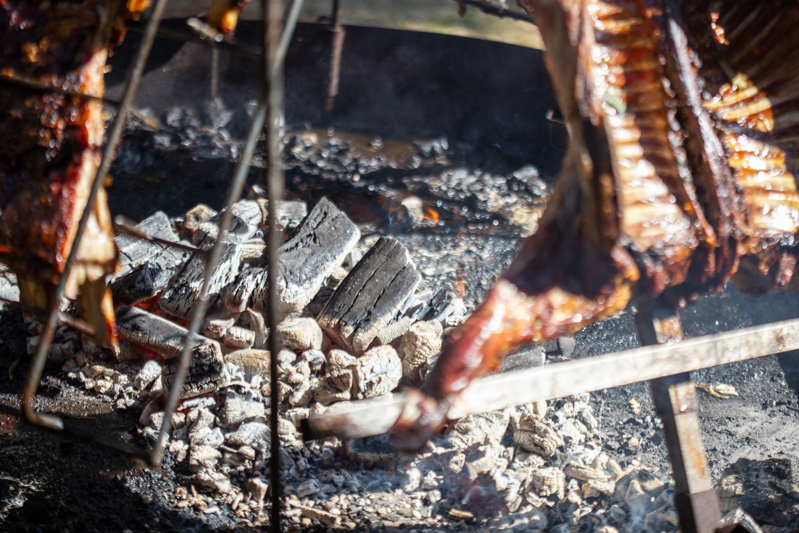 Whole racks of meat on iron crosses leaning over a bed of embers, being basted with a long brush. Photo by Vidal Balielo Jr. on Pexels.