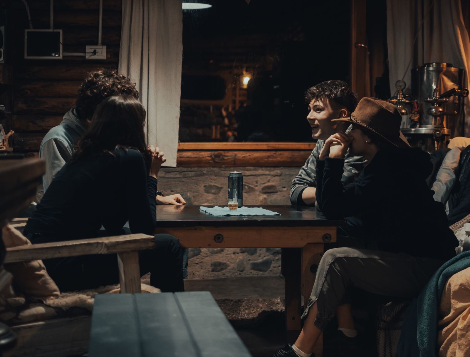 Friends sitting around a table inside a wooden cabin in the evening. Photo by Gaspar Zaldo on Pexels.