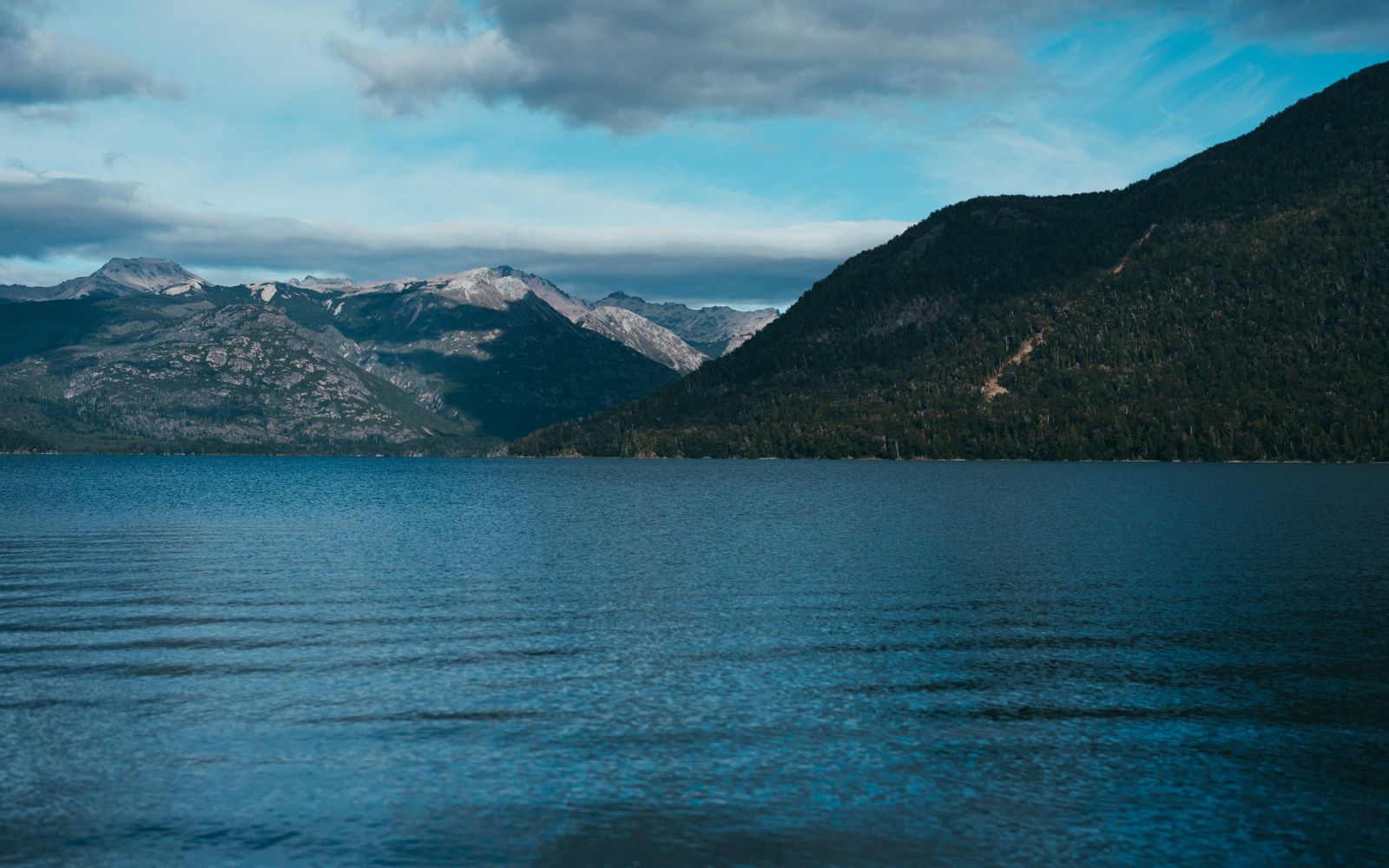Agua de lago azul profundo entre laderas boscosas oscuras bajo nubes bajas. Foto de Guillermo Berlin en Pexels.