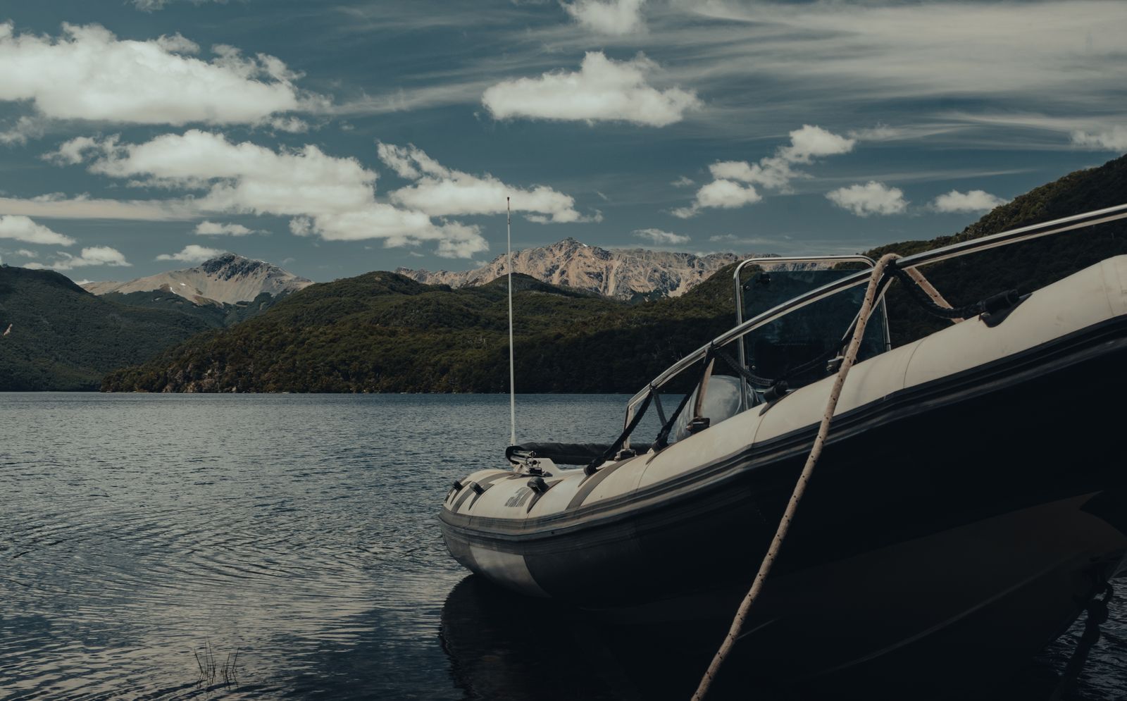 The bow of a boat on open lake water with dark mountains along the far shore. Photo by Gaspar Zaldo on Pexels.