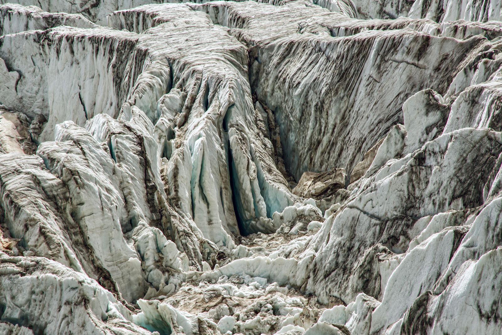 The crevassed grey ice of a glacier, streaked with rock dust. Photo by Susanne Jutzeler, suju-foto on Pexels.