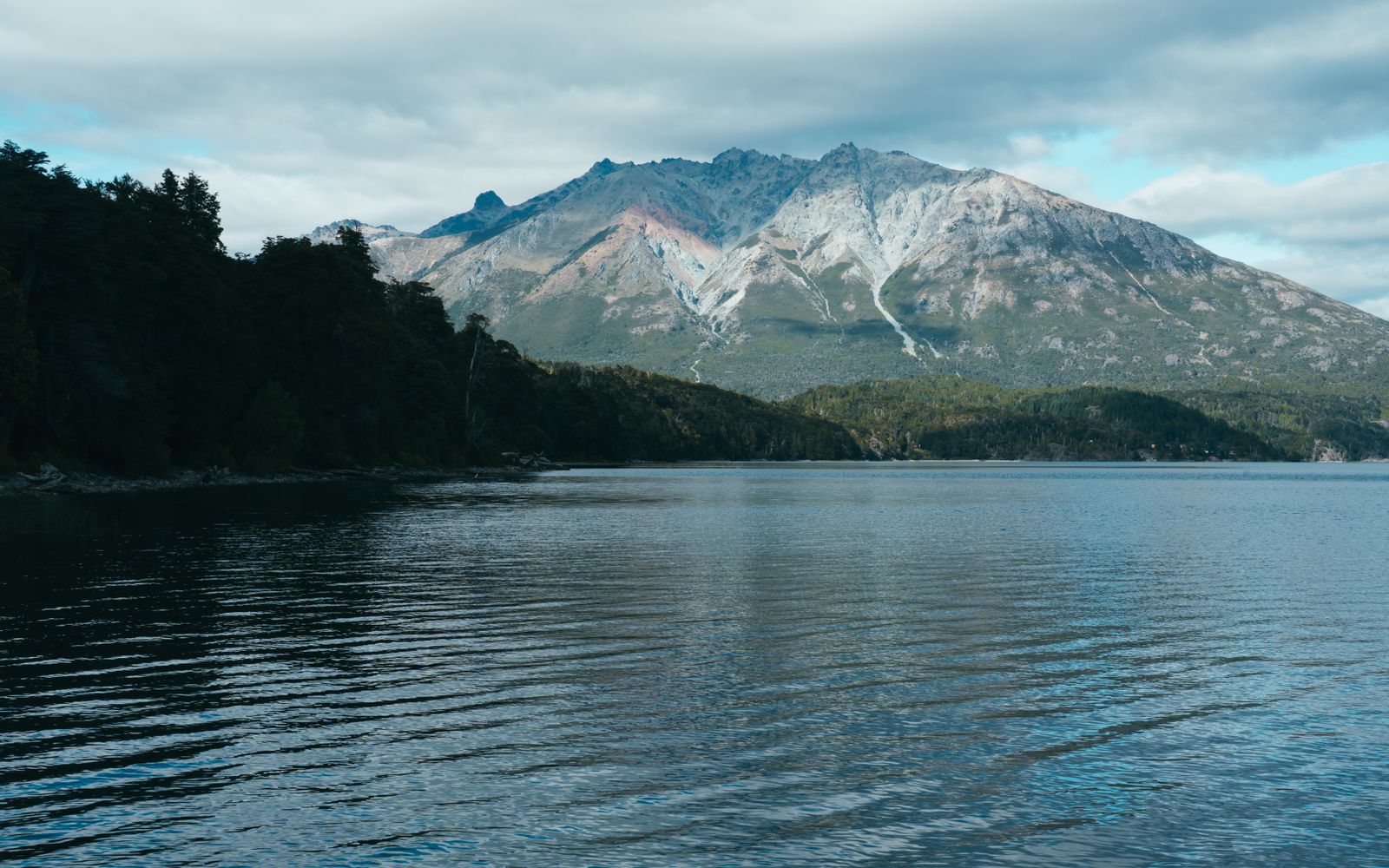 Un lago azul oscuro bajo un pico con vetas de nieve y laderas boscosas empinadas. Foto de Guillermo Berlin en Pexels.