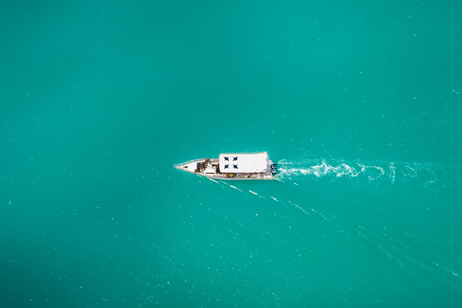 A boat crossing clear turquoise water, seen from above. Photo by Andi saiful Sidik on Pexels.