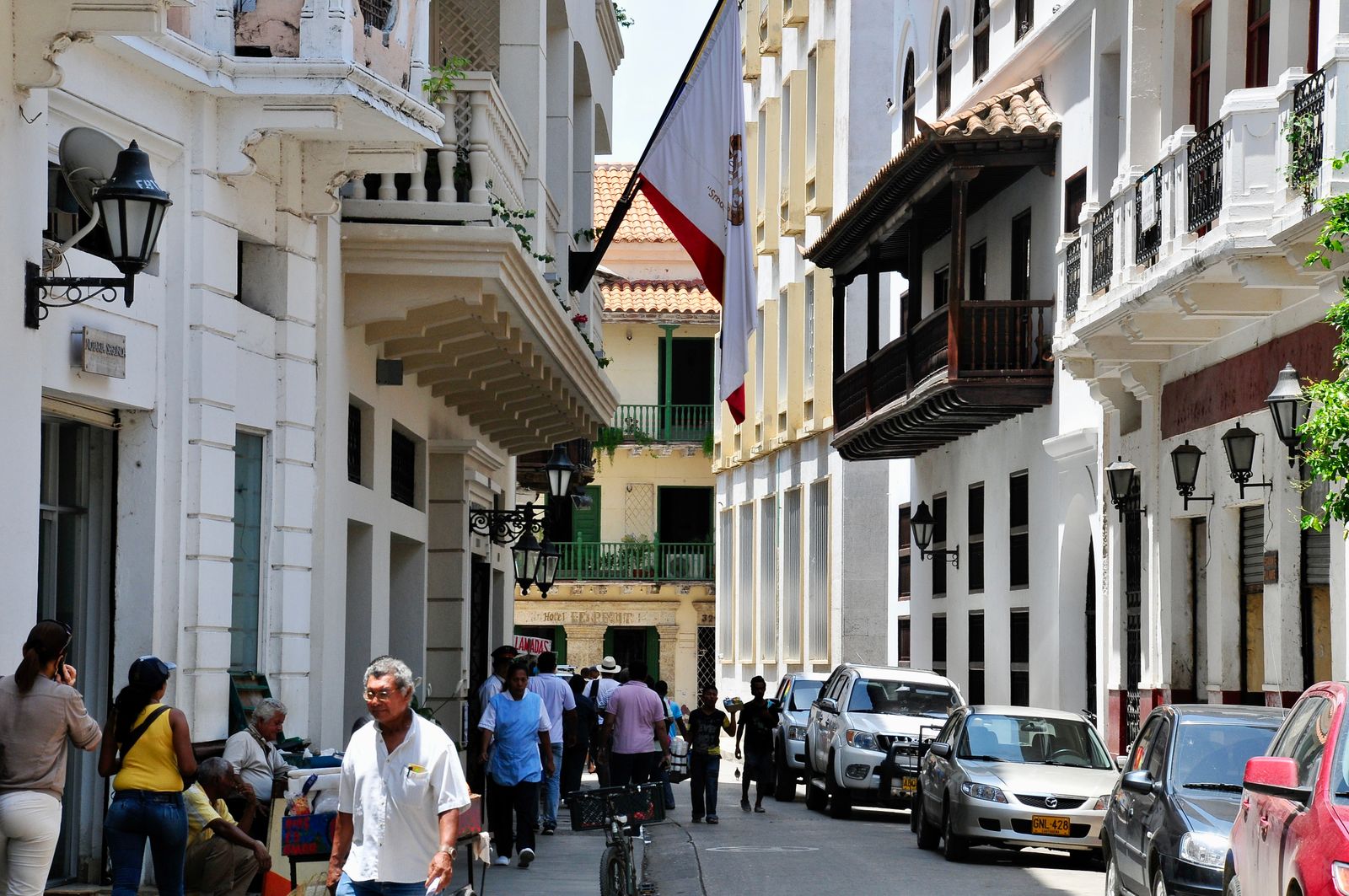 A street in Cartagena's walled city, with balconies, parked cars and people walking. Photo by erik debarre on Pexels.