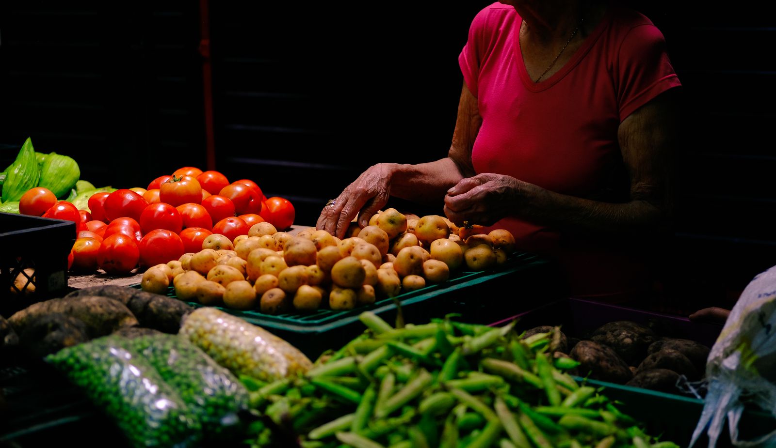 A vendor behind a stall of tomatoes, potatoes and beans at a market in Colombia. Photo by Daniela Perilla on Pexels.