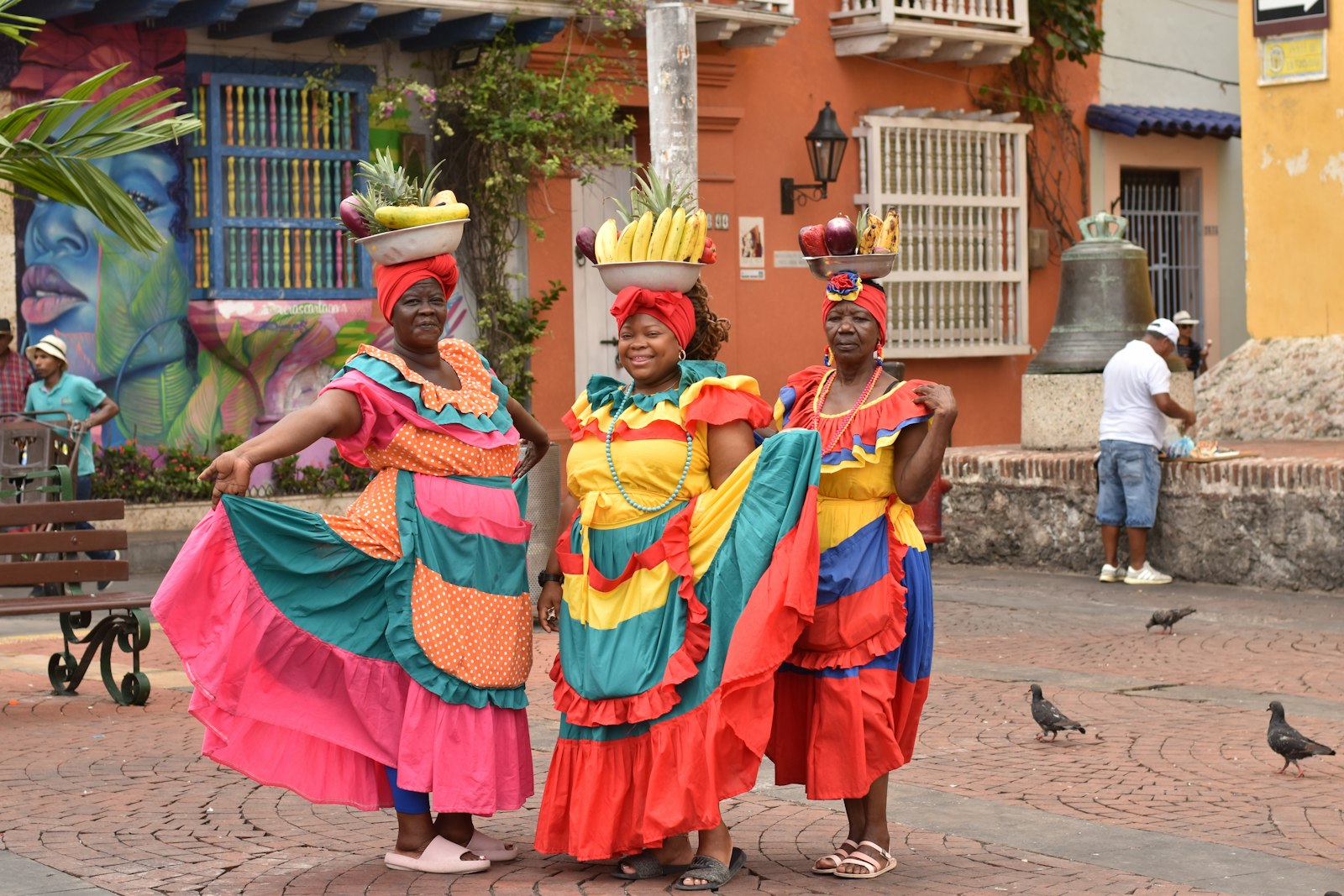 Three palenqueras in ruffled polleras with bowls of fruit, in a plaza in Cartagena. Photo by Tannia Aviles on Unsplash.