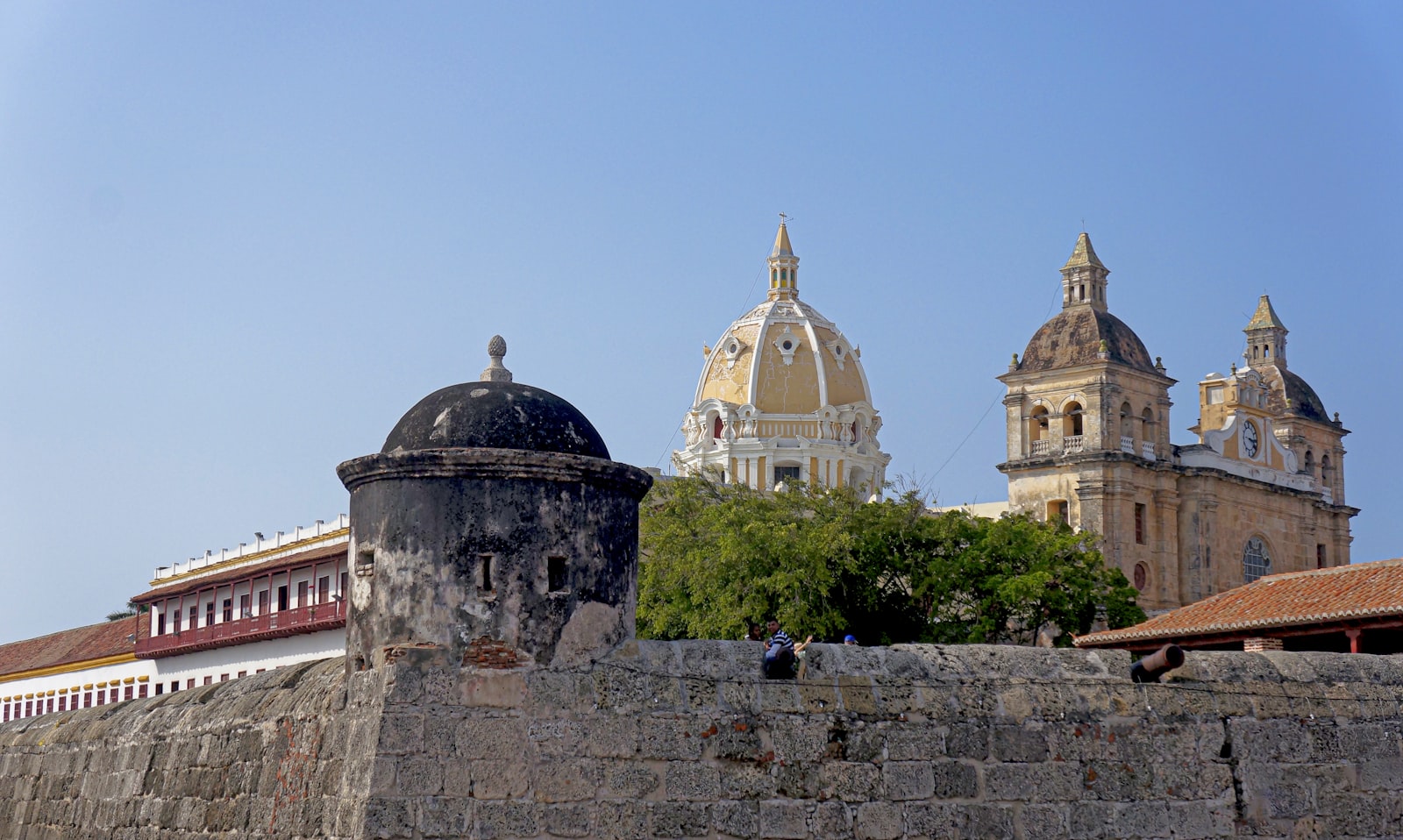 A sentry box on Cartagena's city wall with the domes of San Pedro Claver behind. Photo by Andrés Gómez on Unsplash.