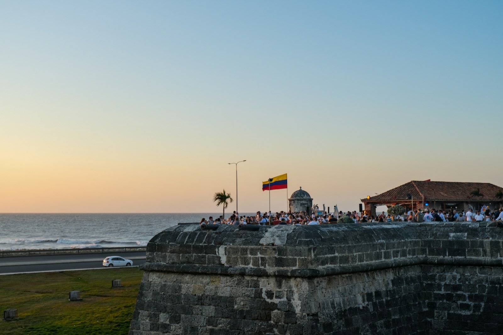 People standing on Cartagena's city wall at sunset beneath the Colombian flag. Photo by Jaime Bishara on Unsplash.