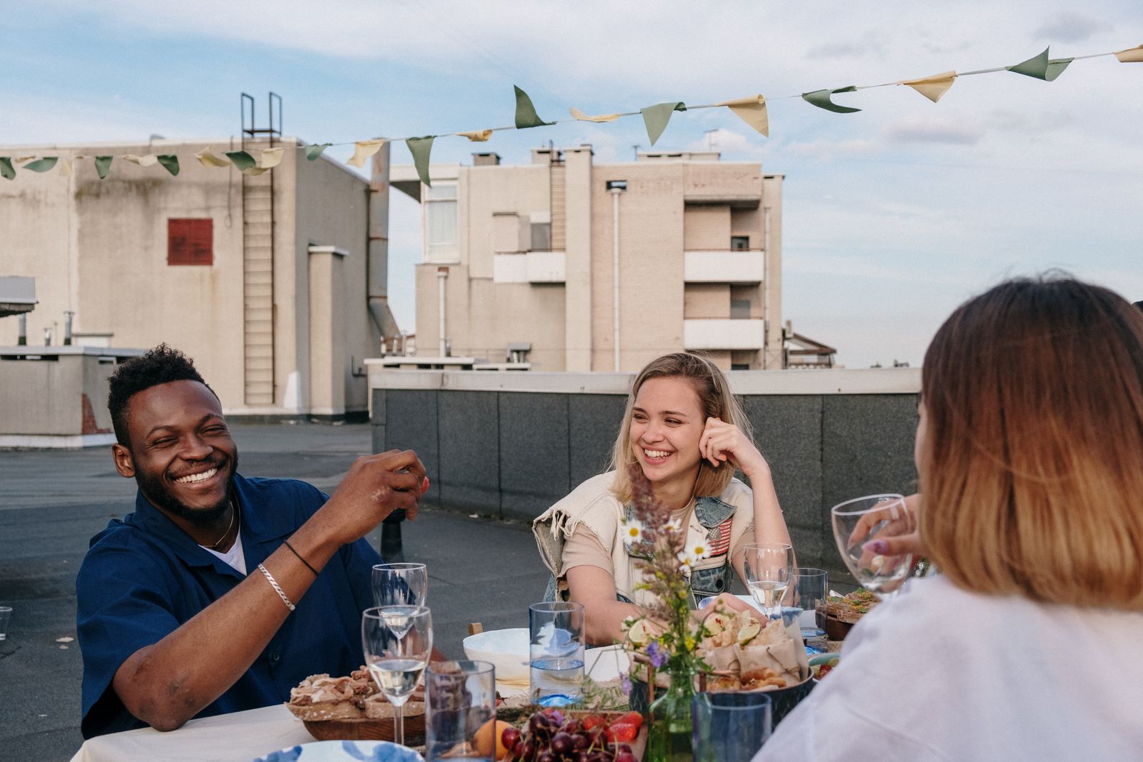 Friends eating and talking around an outdoor table on a rooftop. Photo by cottonbro studio on Pexels.