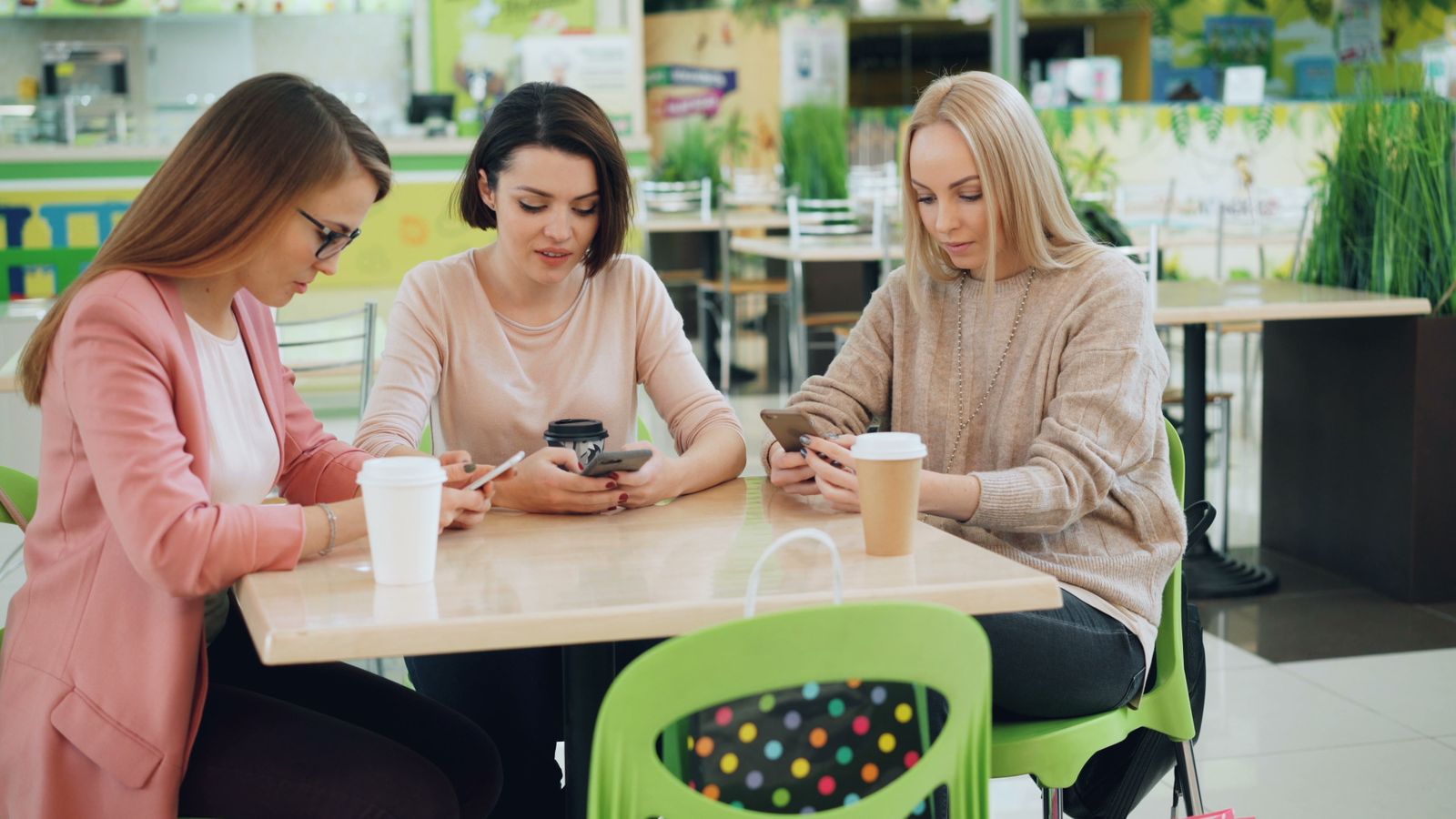 Three friends around a cafe table with coffees and phones, making a plan. Photo by Vitaly Gariev on Pexels.