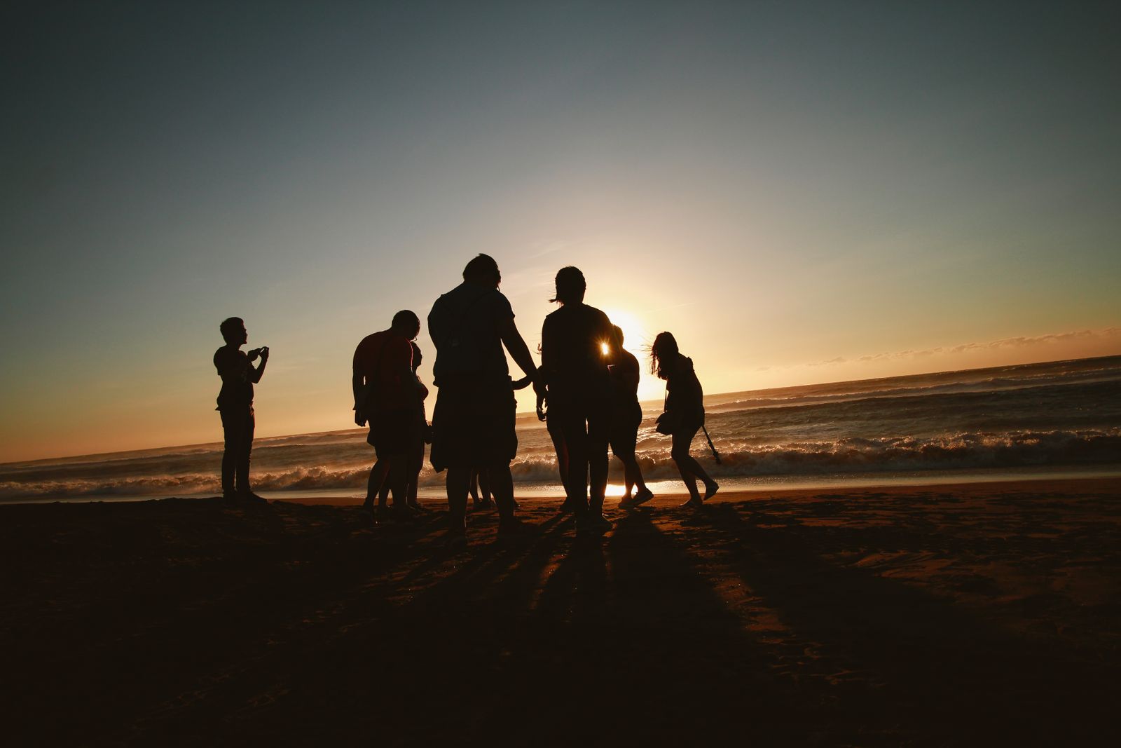 A group of friends silhouetted against the sunset on a beach. Photo by Belle Co on Pexels.