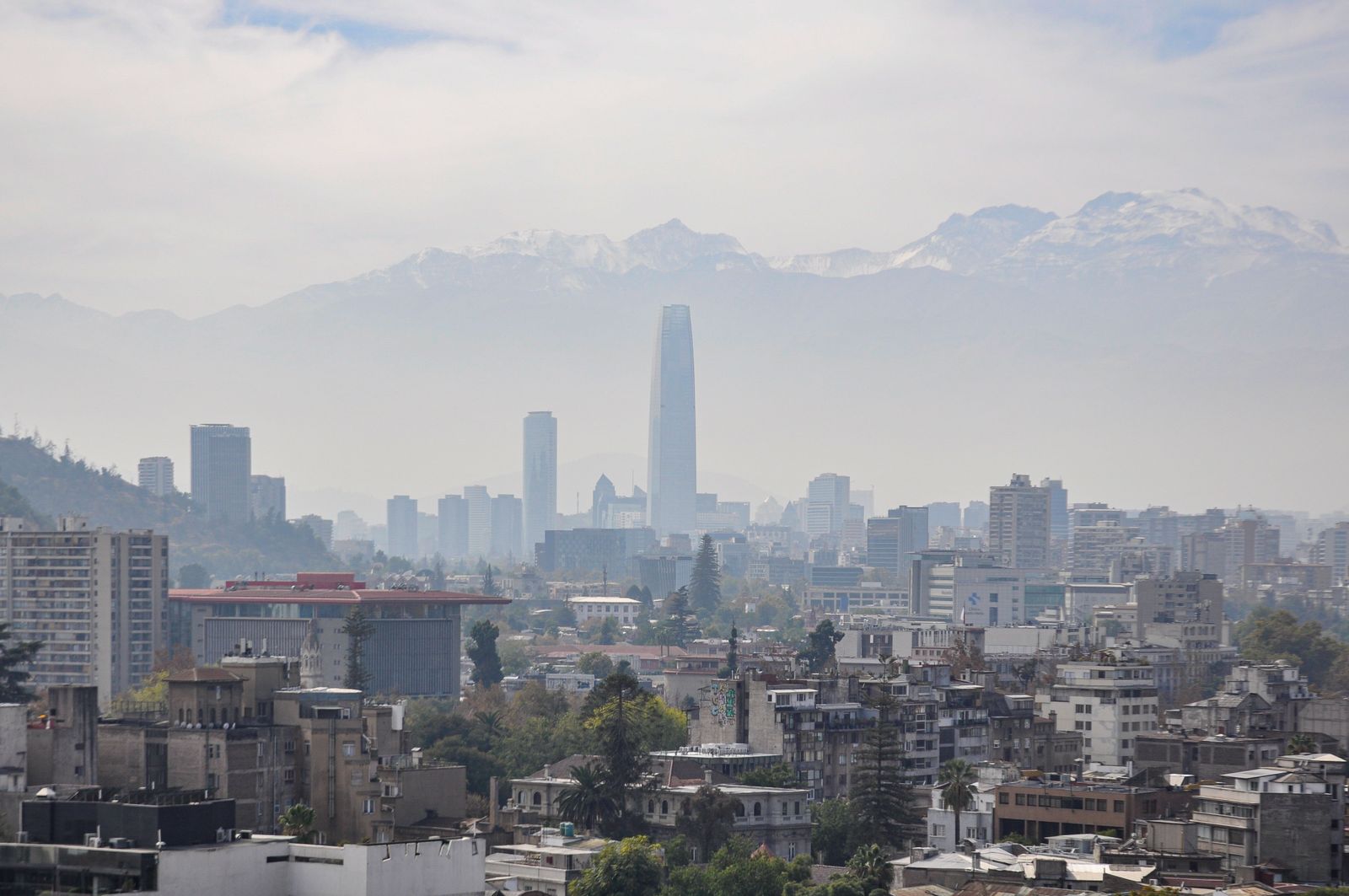 Santiago's towers under a haze, with the snow line of the Andes above the city. Photo by Nikolai Kolosov on Pexels.