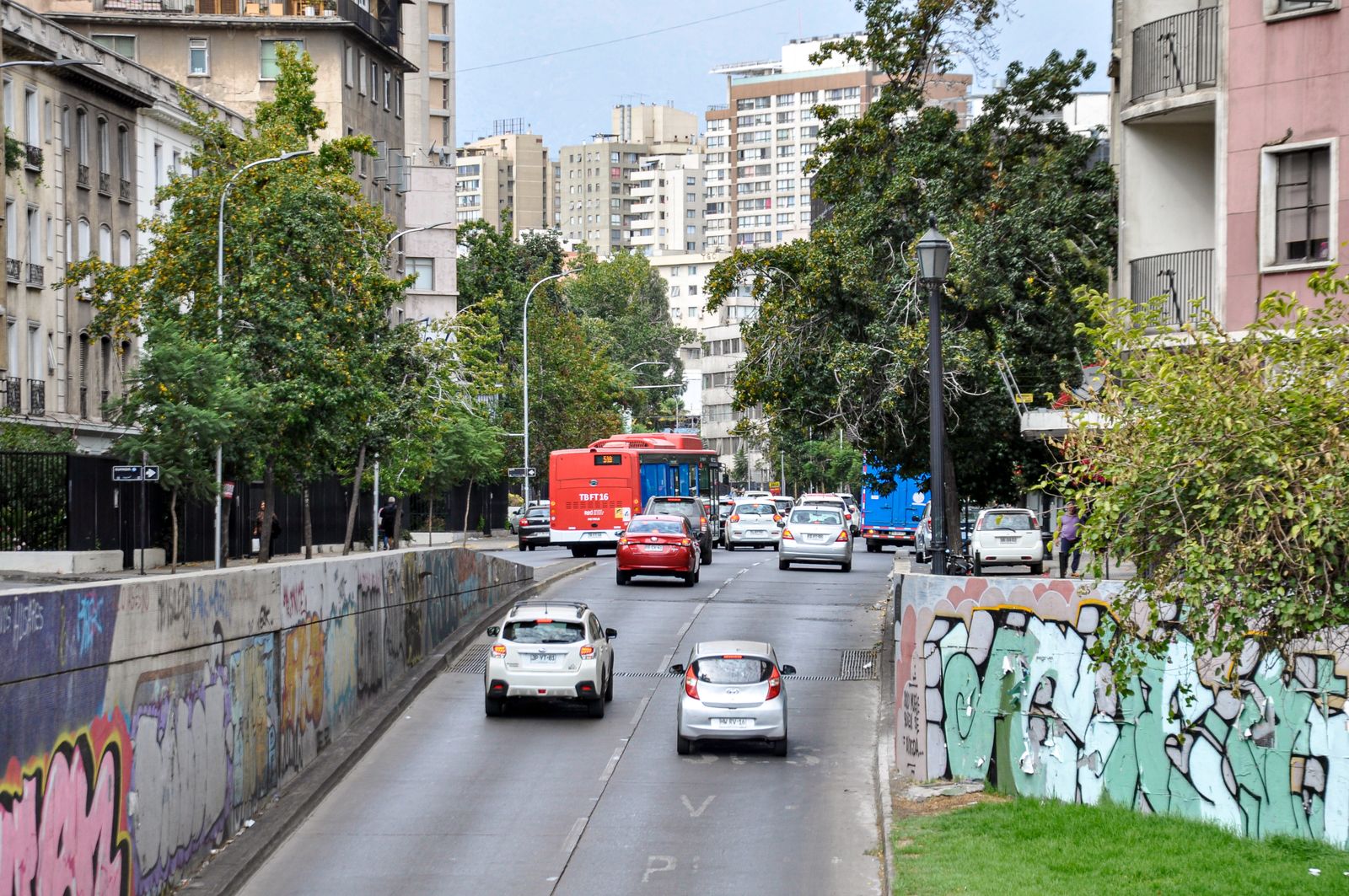 A busy Santiago street with a red city bus and graffitied retaining walls. Photo by Nikolai Kolosov on Pexels.