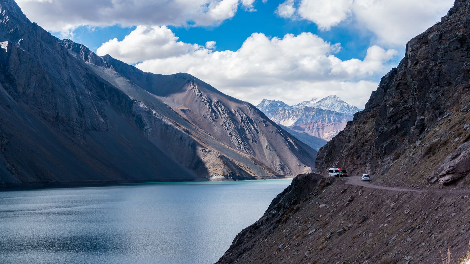 A turquoise reservoir held between bare Andean ridges, with the access road along one side. Photo by Jonathan Santos on Pexels.