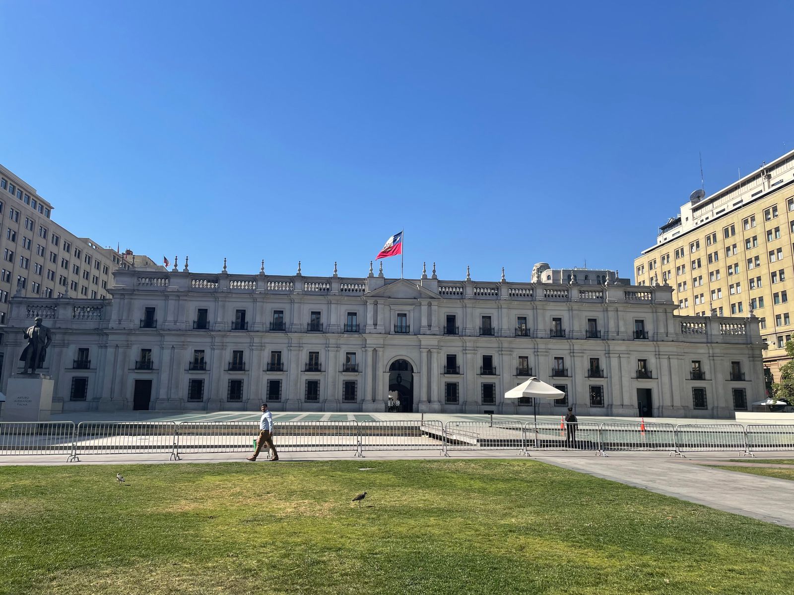 La Moneda palace in Santiago, the Chilean flag flying above the forecourt. Photo by Matheus Natan on Pexels.