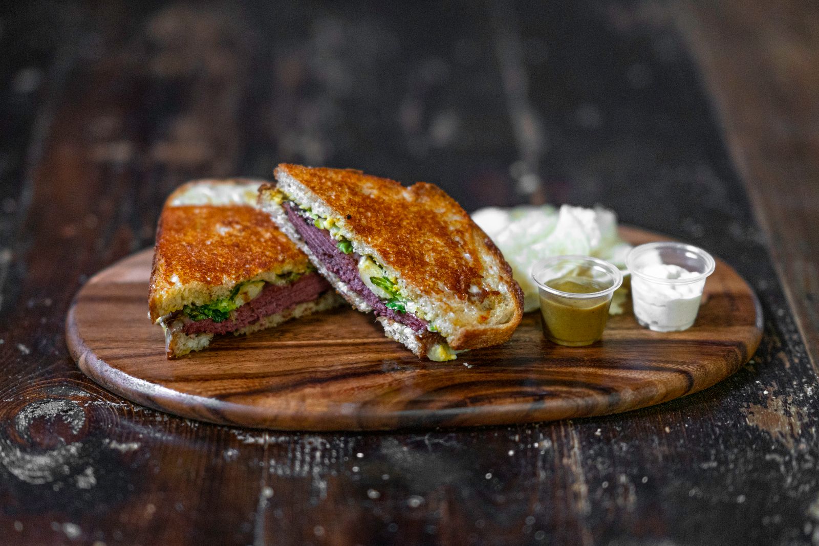 A toasted steak and melted cheese sandwich cut in half on a wooden board. Photo by Daniel Torobekov on Pexels.