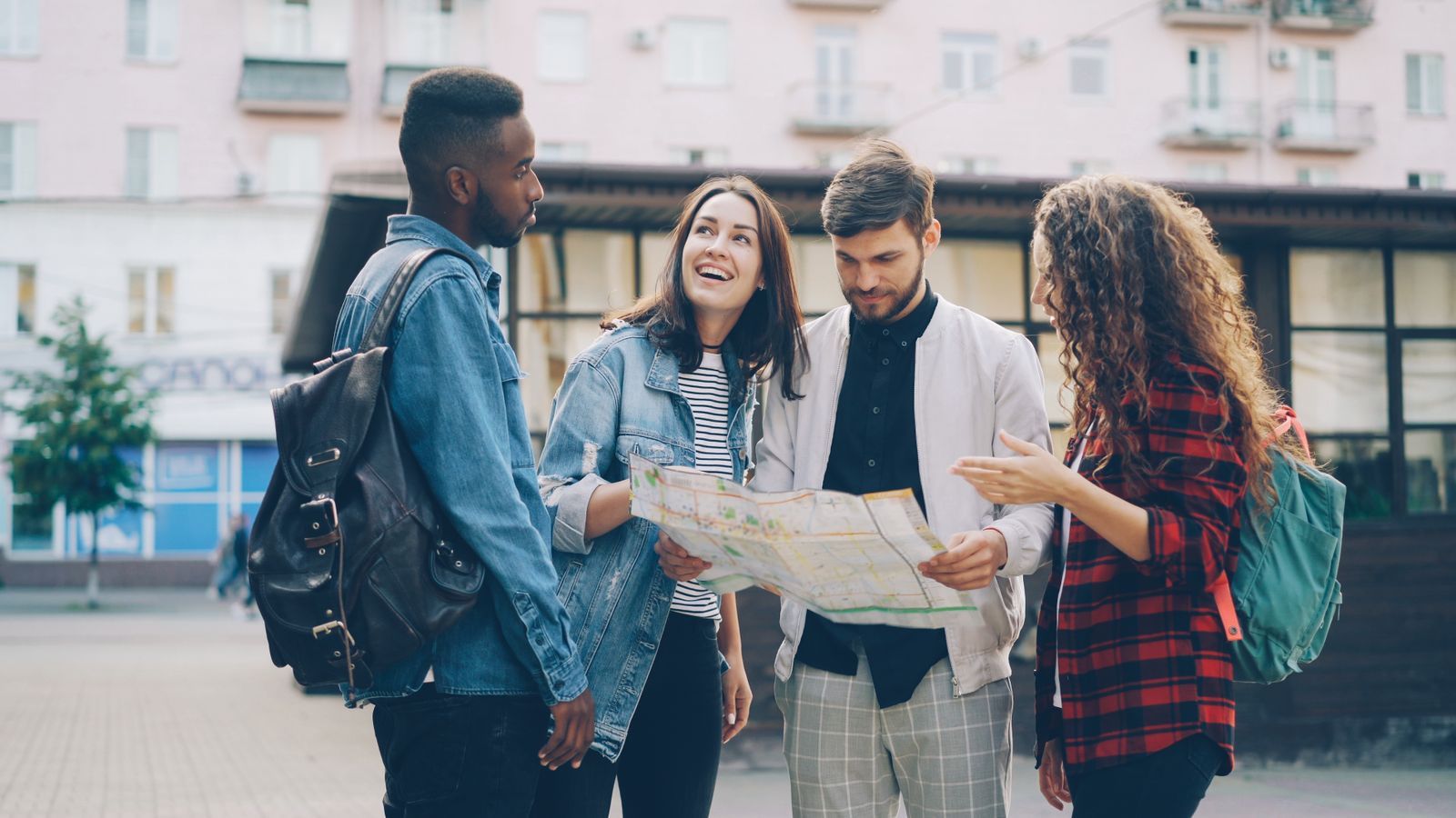 Four friends standing in a street working out a paper map together. Photo by Vitaly Gariev on Pexels.