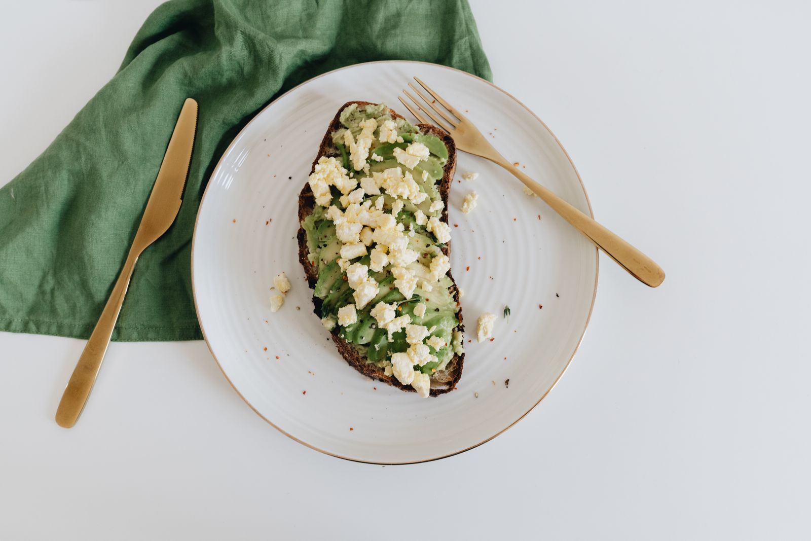 A slice of bread topped with avocado and crumbled cheese on a plate. Photo by alleksana on Pexels.