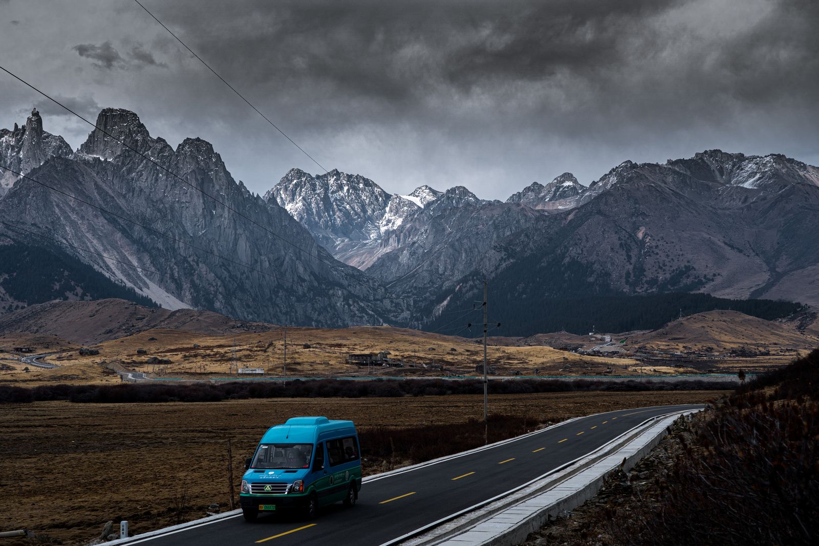 A small van on an empty road below a dark snow-dusted mountain range. Photo by 李 玄萌 on Pexels.