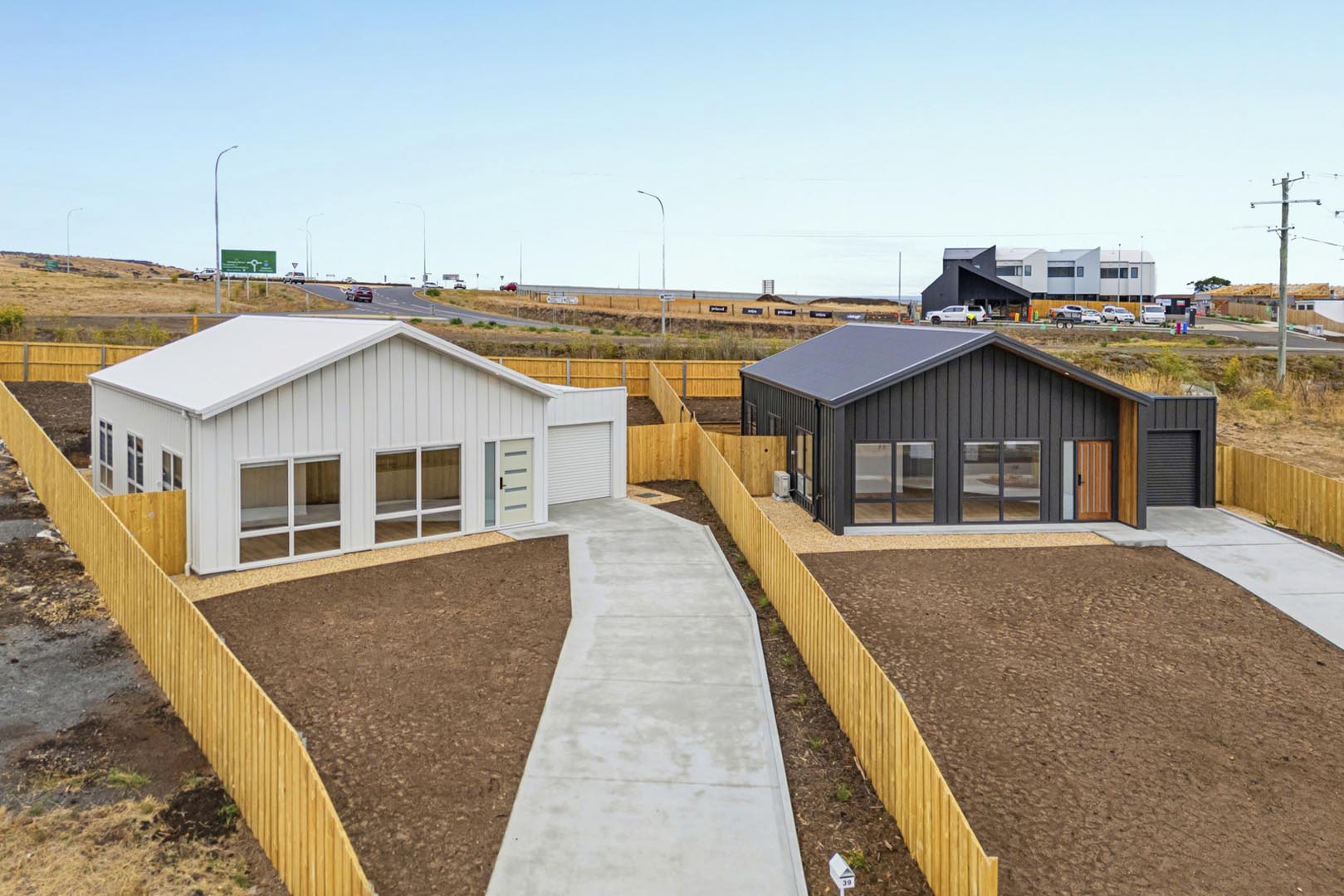 Two modern single-story houses with fenced yards, concrete driveways, and dry soil in front yards.