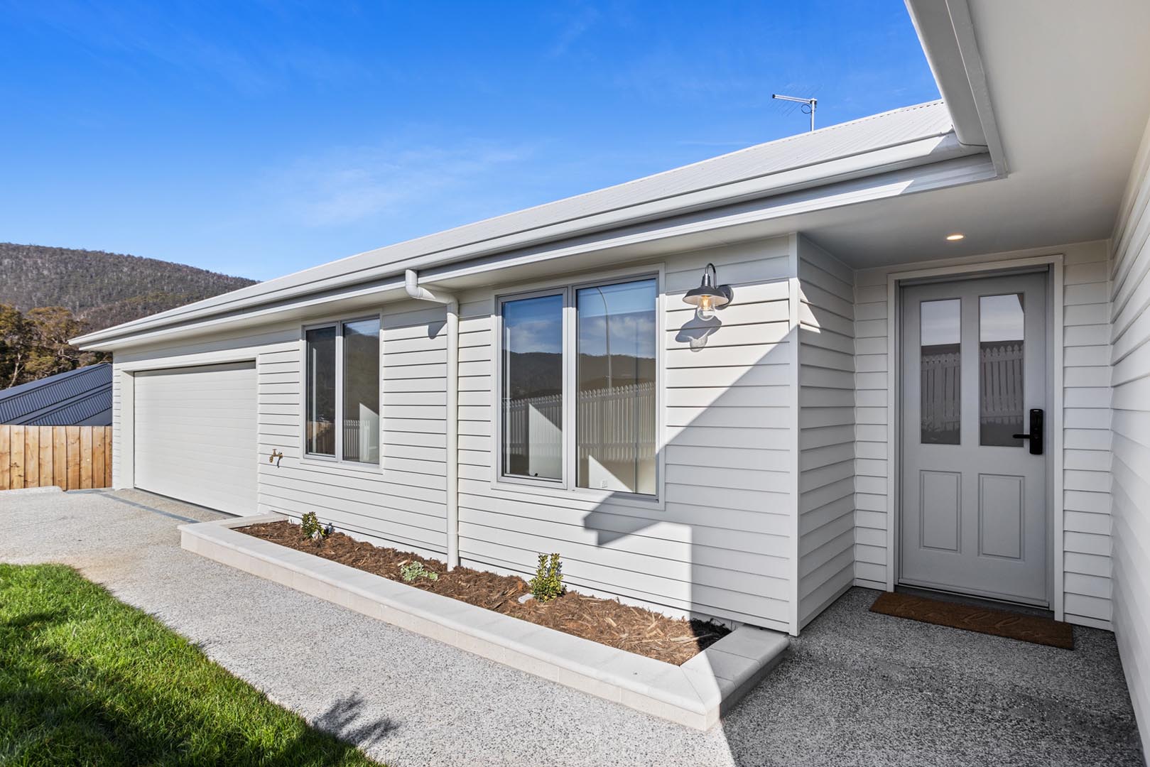 Modern white house exterior with garage, two windows, a front door, and a small garden bed.
