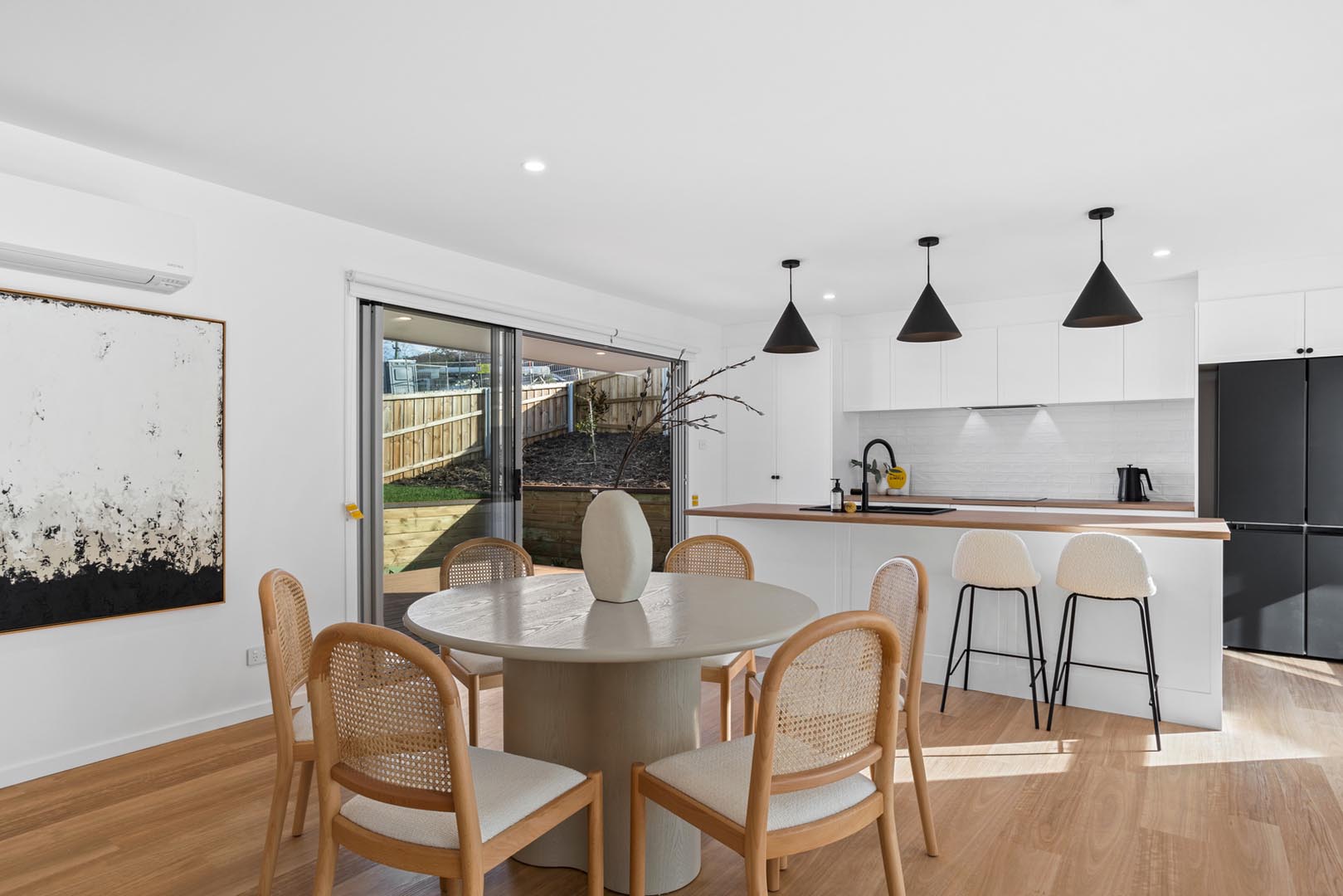 Modern kitchen and dining area with round table, wooden chairs, white island, and black pendant lights.
