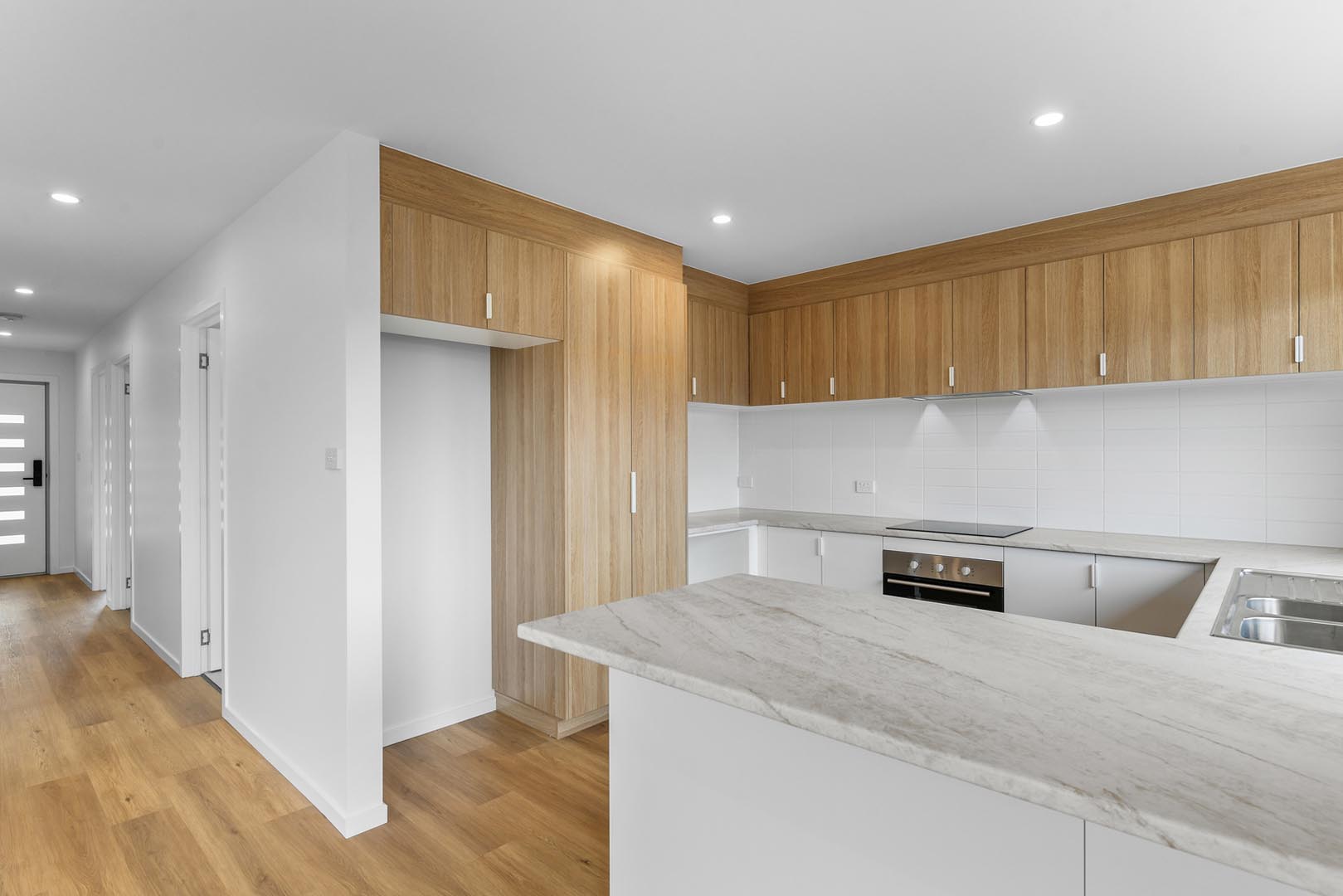 Modern kitchen with wood cabinets, white marble countertops, built-in oven, and a stainless steel sink.