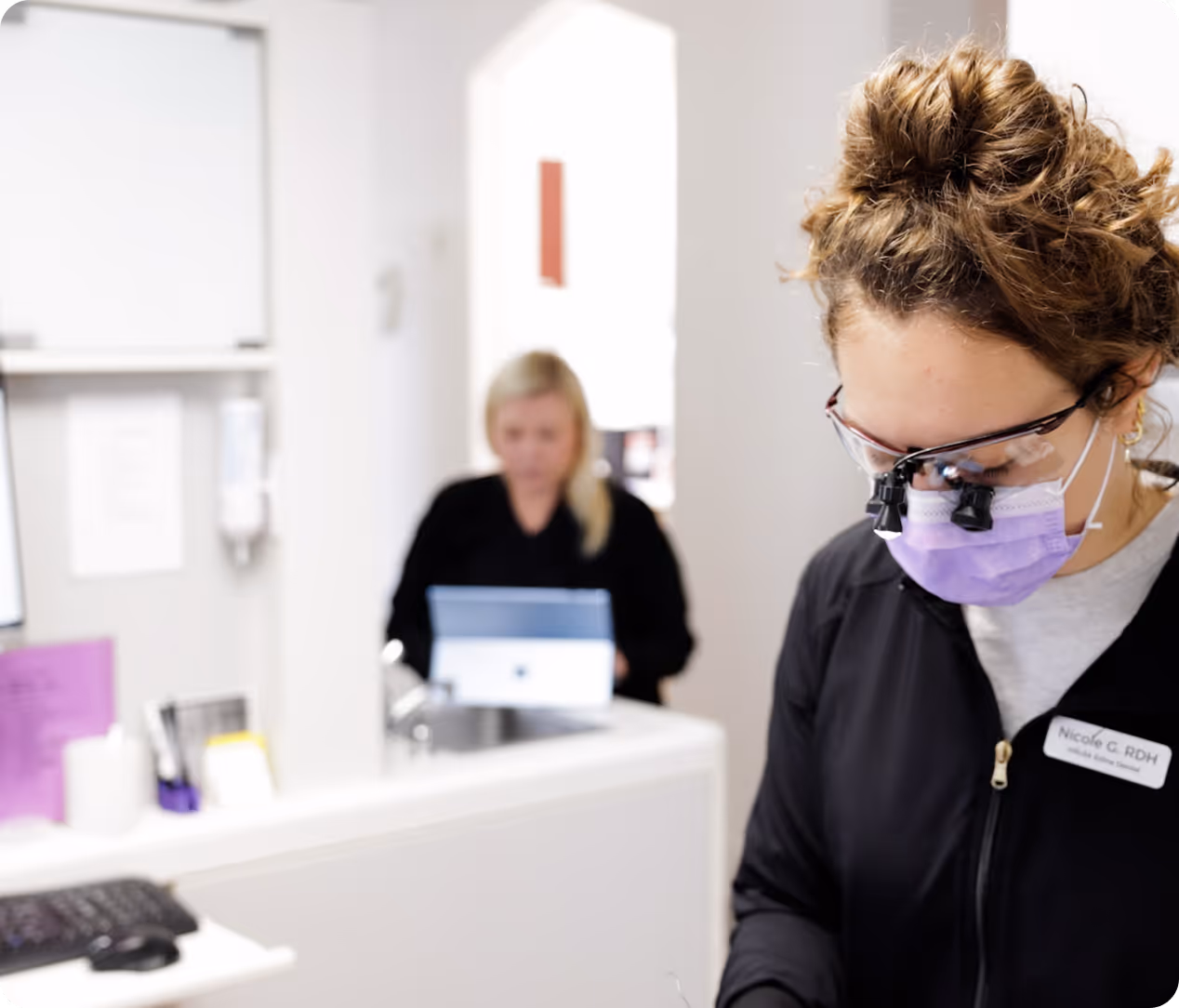 Dental hygienist wearing magnifying glasses and mask, focused on work in a clinical setting.