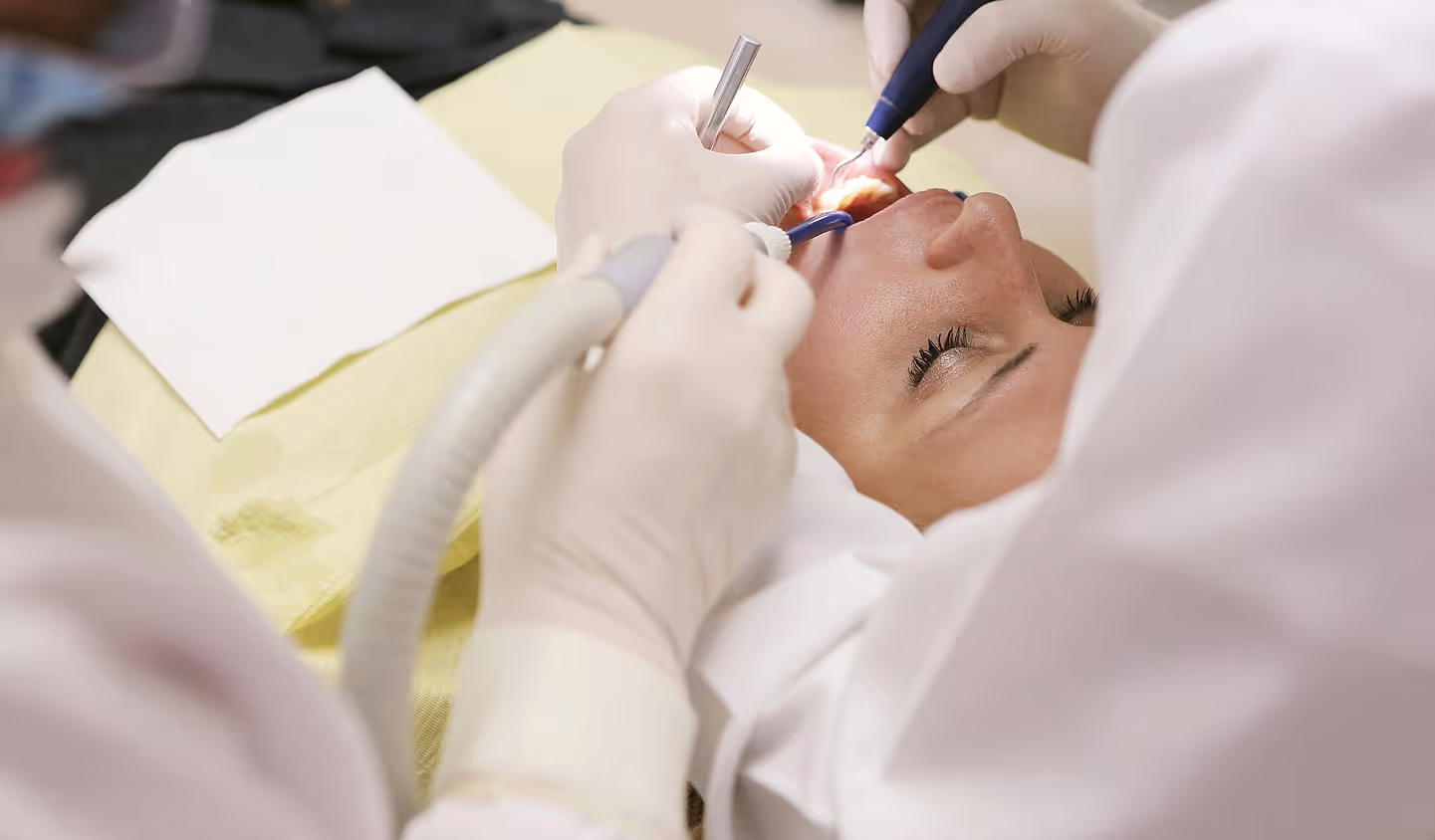 Dentist using dental tools to examine and treat a patient lying back with mouth open.