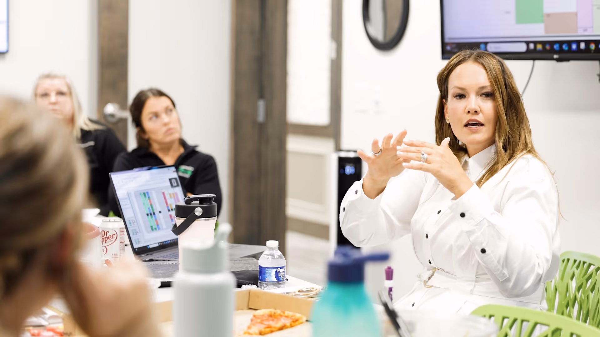 Woman in white shirt speaking during a meeting with others listening and laptop on the table.