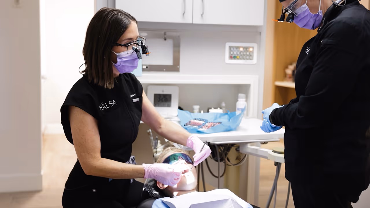 Two dental professionals in masks treating a patient lying back in a dental chair.