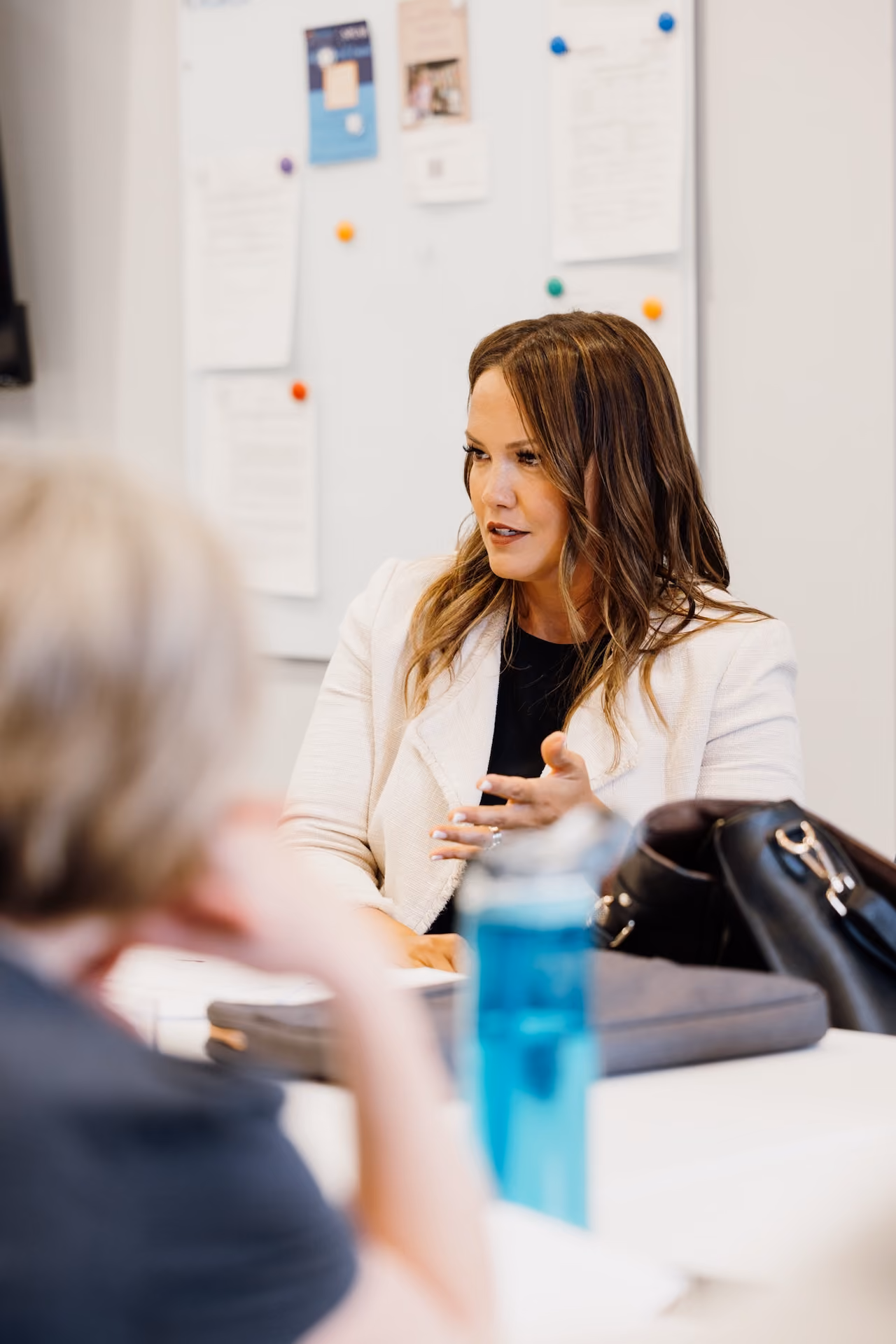 Woman in white blazer speaking during a meeting with another person in an office.
