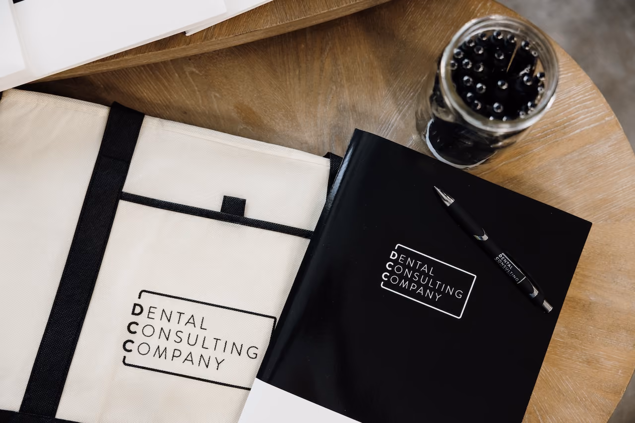 White and black folders labeled 'Dental Consulting Company' with a pen and glass of black pens on wooden table.