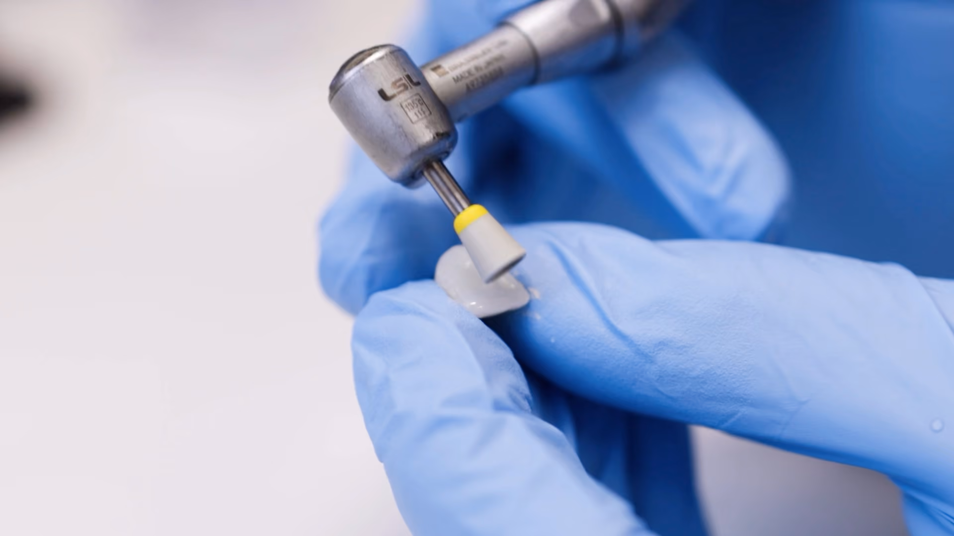 Gloved hands holding dental tool polishing a dental veneer or crown.