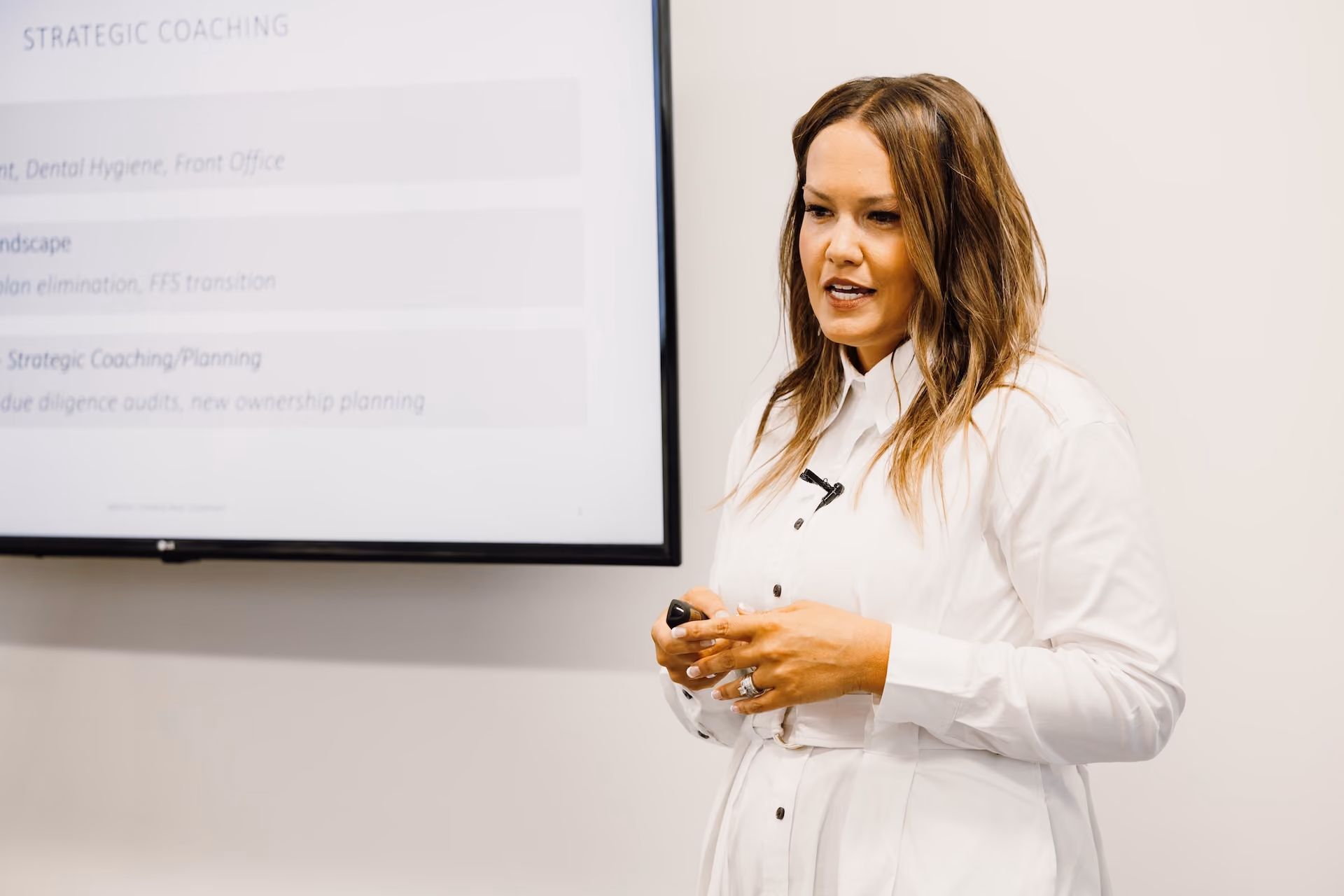 Woman in white shirt giving a presentation with a screen showing strategic coaching text in background.
