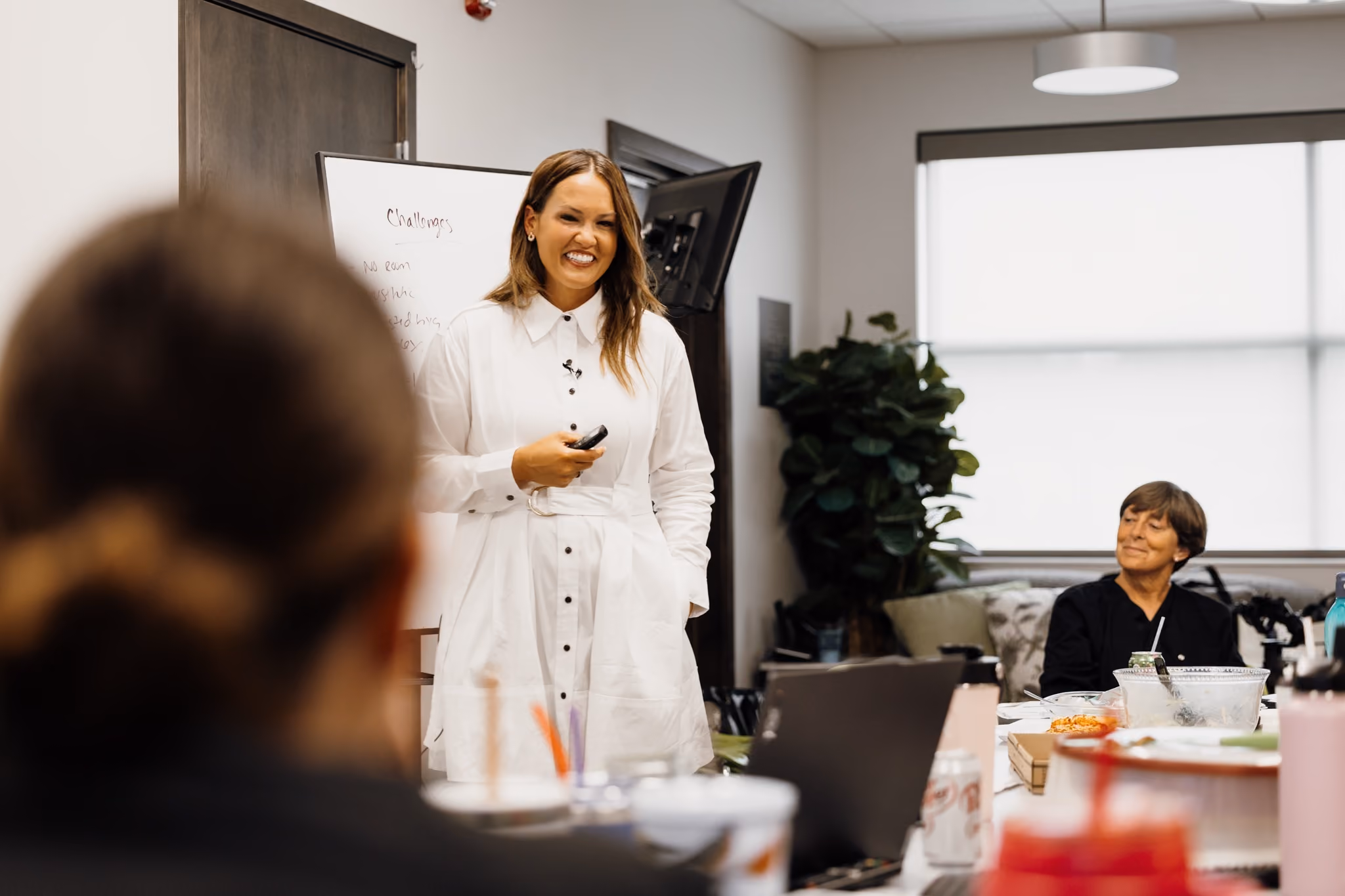 Woman in white dress presenting in a meeting room with seated colleagues around a table.