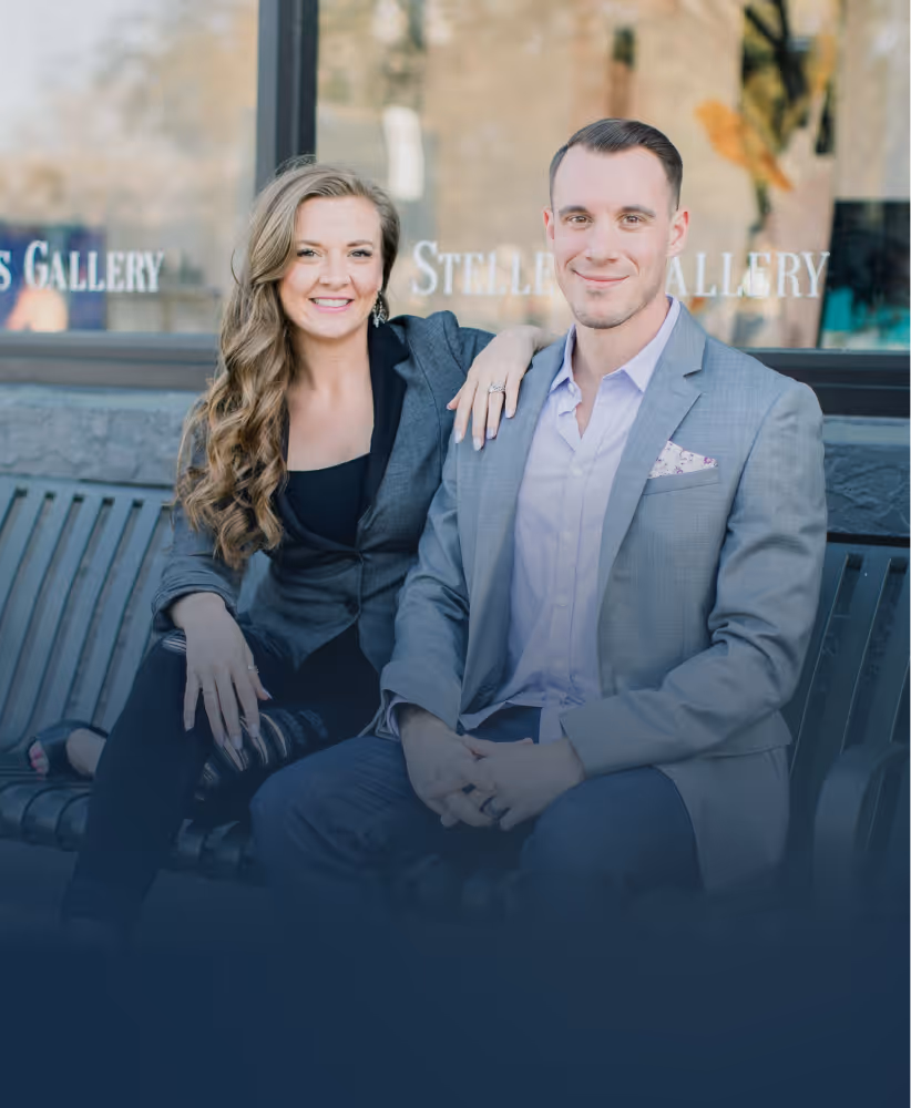 Smiling man and woman in business attire sitting on a bench outside a gallery.