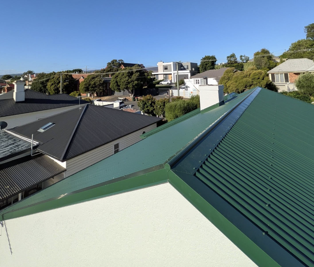 View of residential neighborhood with green and black corrugated metal roofs under a blue sky.