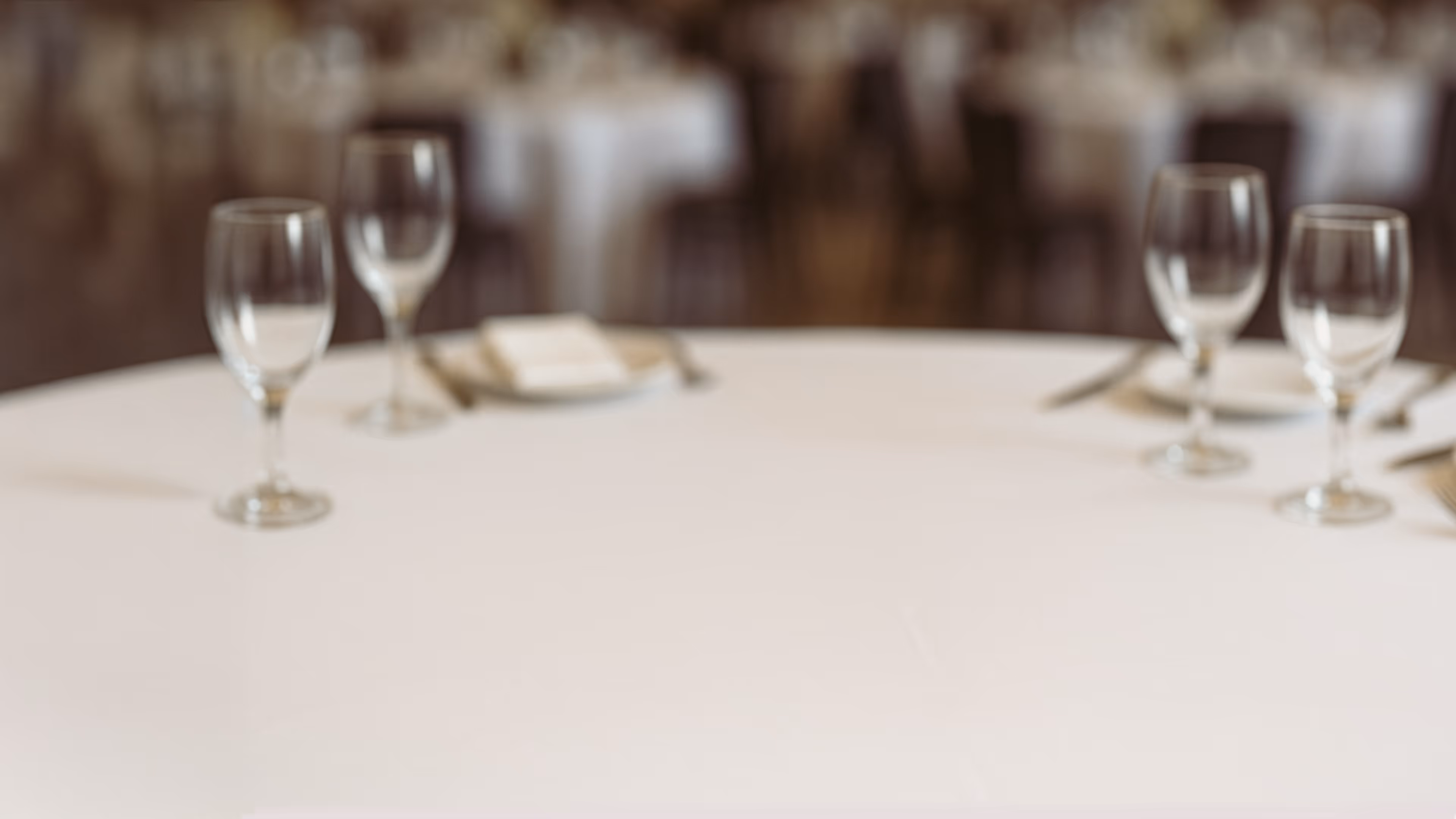 Round table set with empty wine glasses and white tablecloth in a softly lit restaurant.