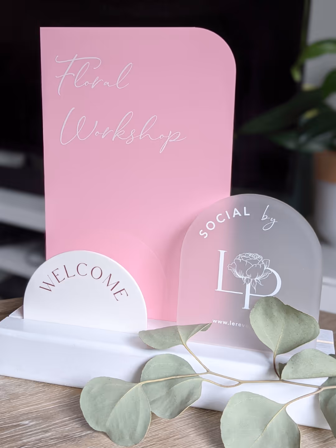 Pink and white floral workshop welcome signs with green leaves on a wooden table.