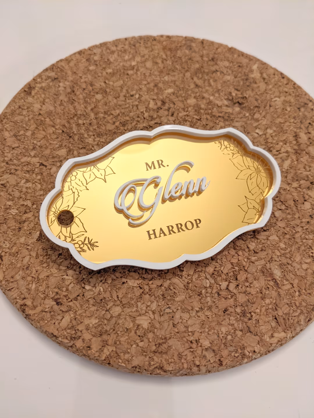 Gold-colored decorative name tag reading 'Mr. Glenn Harrop' on a round cork mat.