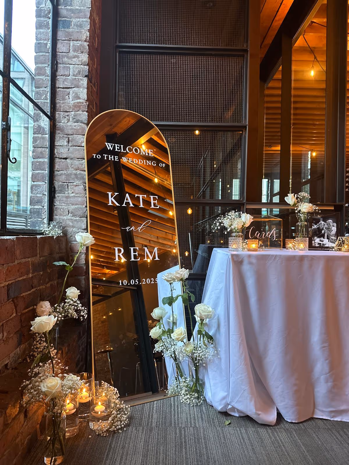 Mirror wedding sign for Kate and Rem on 10.05.2025, surrounded by white roses and candles.