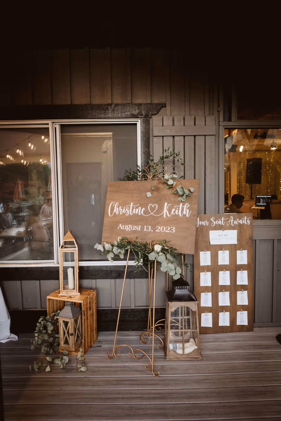 Wooden wedding signs for Christine and Keith dated August 13, 2023, with lanterns and greenery decor.
