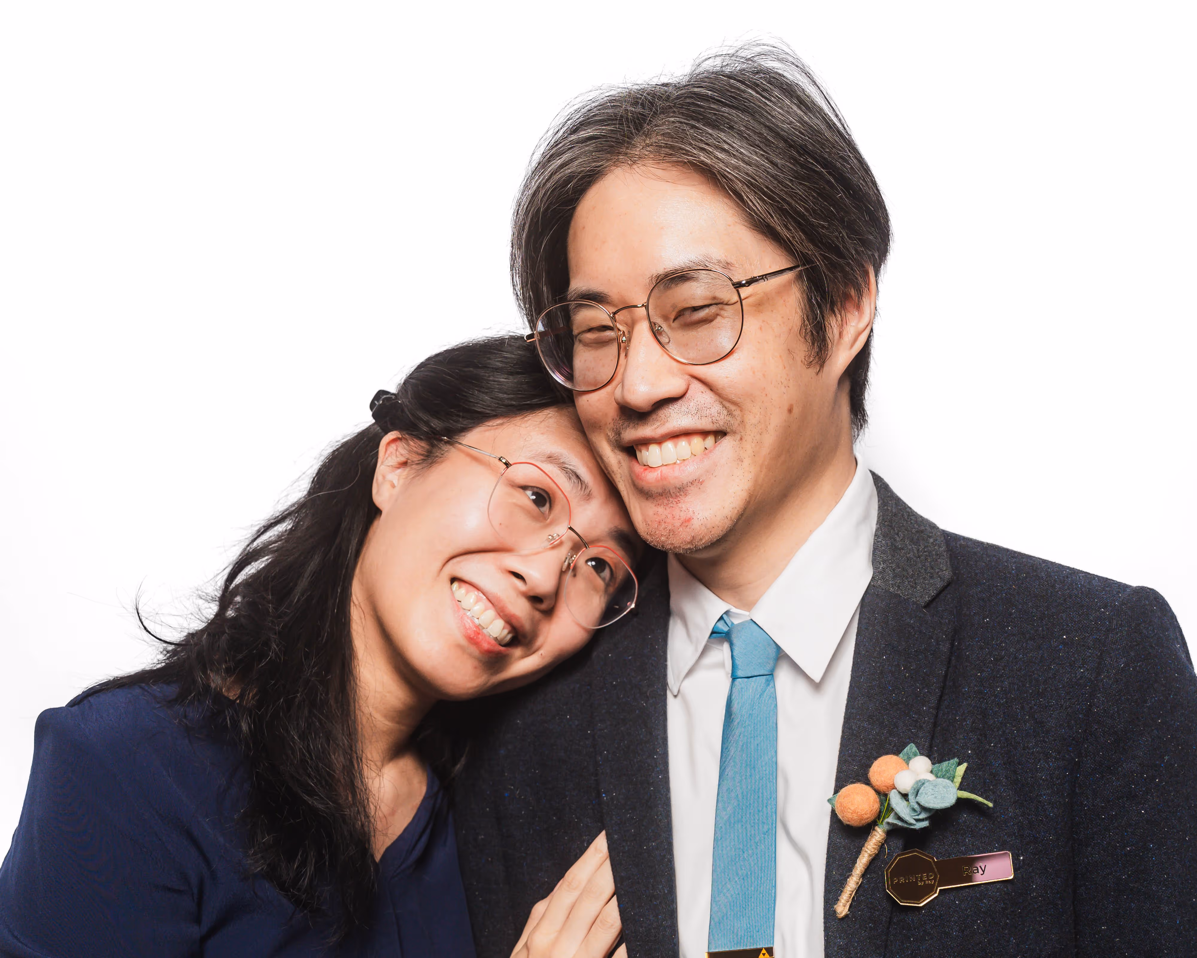 Smiling couple with glasses, woman resting head on man's shoulder, man wearing suit and blue tie.